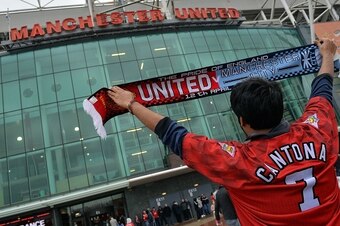 A supporter poses for a photograph holding a 'half-and-half' Manchester United and Manchester City scarf ahead of the English Premier League football match between Manchester United and Manchester City at Old Trafford in Manchester, north west England on 