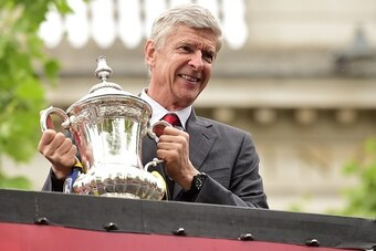 Arsenal's French manager Arsene Wenger holds the trophy from the top deck of an open-topped bus during the Arsenal victory parade in London on May 31, 2015, following their win in the English FA Cup final football match on May 30, 2014 against Aston Villa