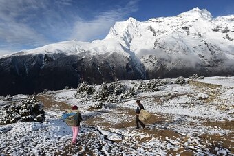 Basanti (L), 14, and her friend Jhalijhsa, 14, walk with their empty baskets down to the north-eastern Nepalese town of Namche Bazar (unseen) on a freshly snow-dusted field near Mt. Kondge (R) on April 18, 2015. Basanti and Jhalijsha were heading to the m