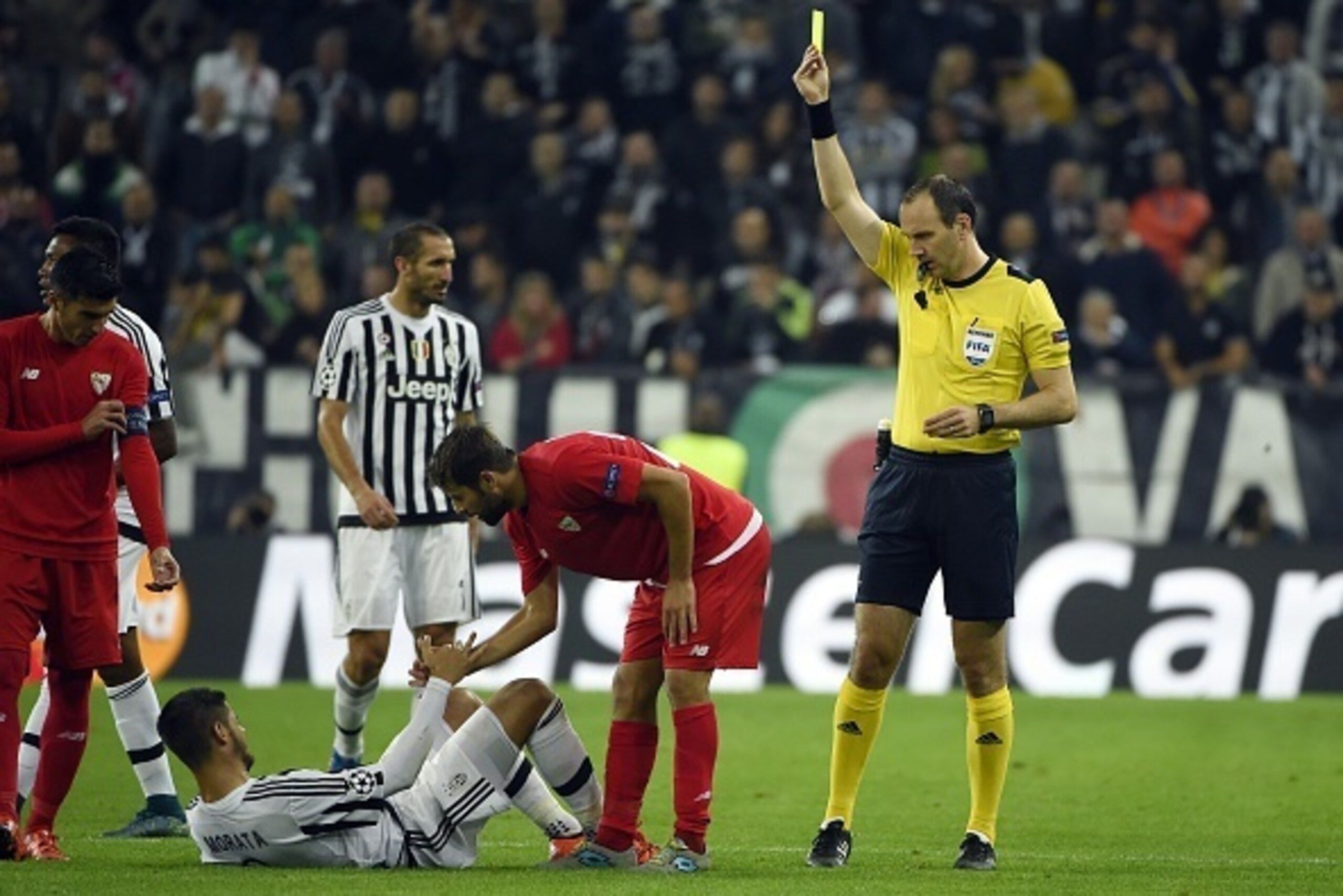 Sevilla's defender Coke (C) receives a yellow card from referee Jonas Eriksson after a tackle on Juventus' forward from Spain Alvaro Morata during the UEFA Champions League football match Juventus vs FC Sevilla on September 30 at the Juventus stadium in T