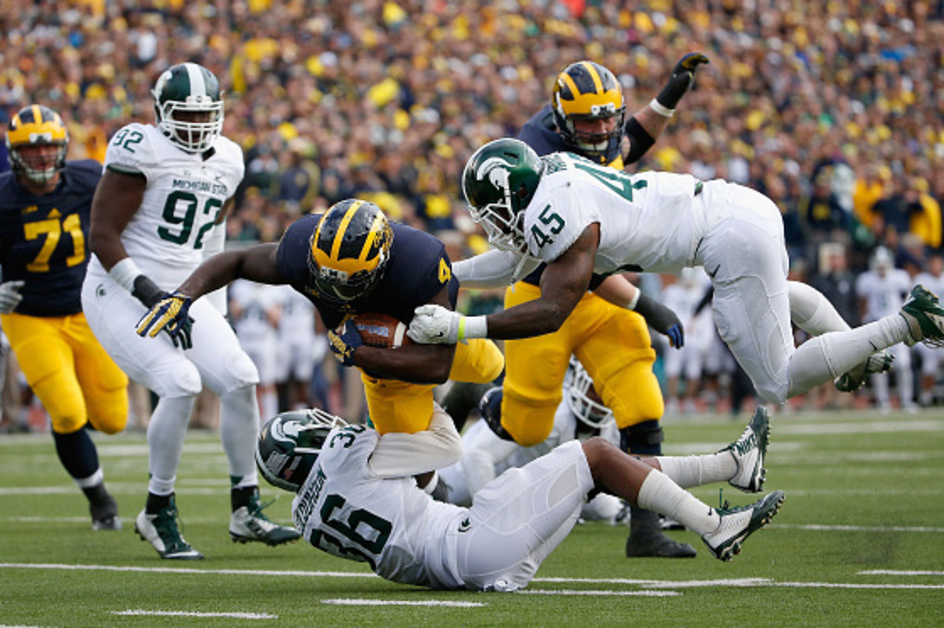 ANN ARBOR, MI - OCTOBER 17:  Running back De'Veon Smith #4 of the Michigan Wolverines is tackled by cornerback Arjen Colquhoun #36 and linebacker Darien Harris #45 of the Michigan State Spartans during the second quarter of the college football game at Mi