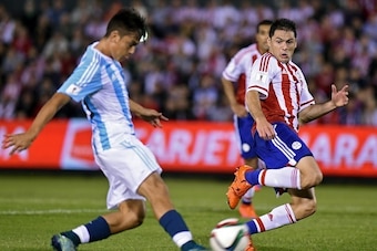 Argentina's forward Paulo Dybala (L) kicks the ball as Paraguay's Pablo Cesar Aguilar looks on during their Russia 2018 FIFA World Cup South American Qualifiers football match, at the Defensores del Chaco stadium in Asuncion, on October 13, 2015.    AFP P