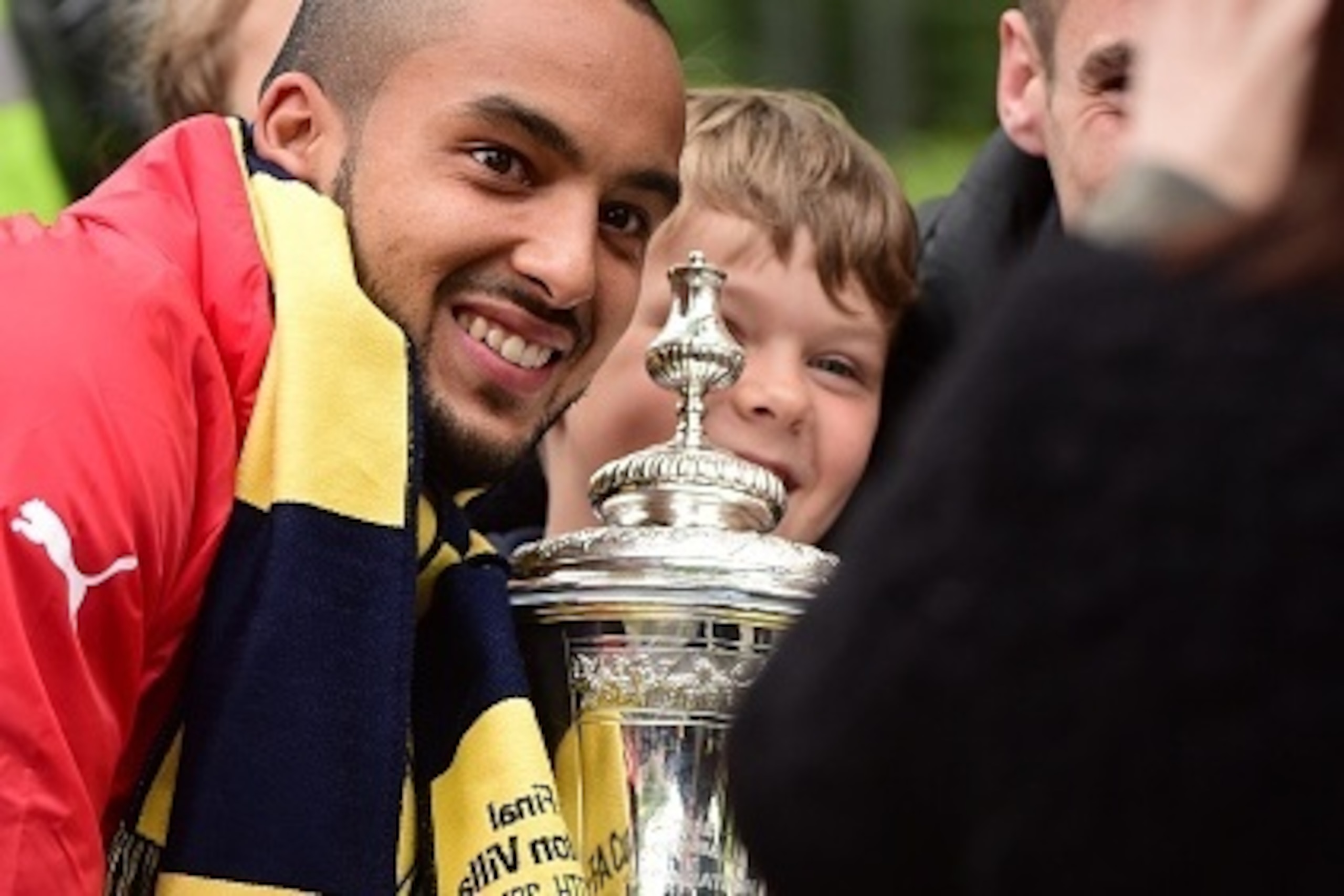 Arsenal's English midfielder Theo Walcott (L) holds the trophy as he poses for a photograph with a fan during the Arsenal victory parade in London on May 31, 2015, following their win in the English FA Cup final football match on May 30, 2014 against Asto