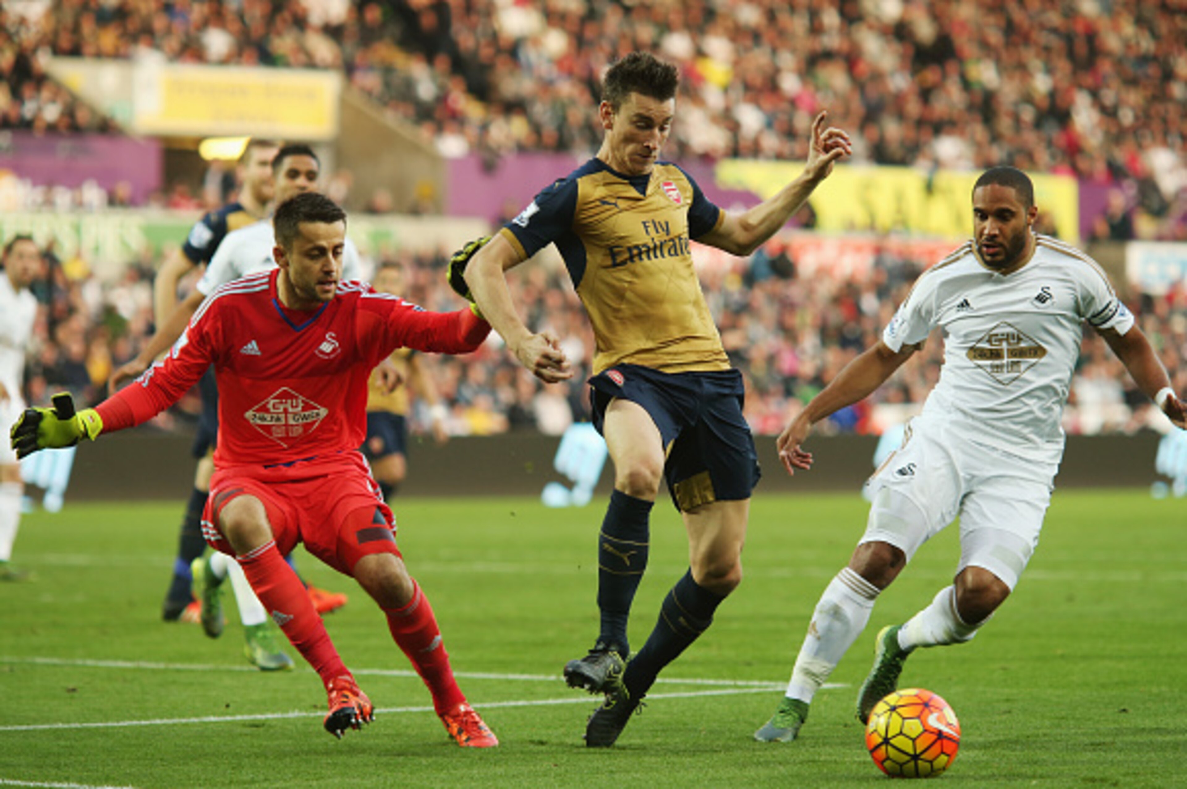 SWANSEA, WALES - OCTOBER 31: Laurent Koscielny (C) of Arsenal competes for the ball against Lukasz Fabianski (L) and Ashley Williams (R) of Swansea City during the Barclays Premier League match between Swansea City and Arsenal at Liberty Stadium on Octob SWANSEA, WALES - OCTOBER 31: Laurent Koscielny (C) of Arsenal competes for the ball against Lukasz Fabianski (L) and Ashley Williams (R) of Swansea City during the Barclays Premier League match between Swansea City and Arsenal at Liberty Stadium on Octob