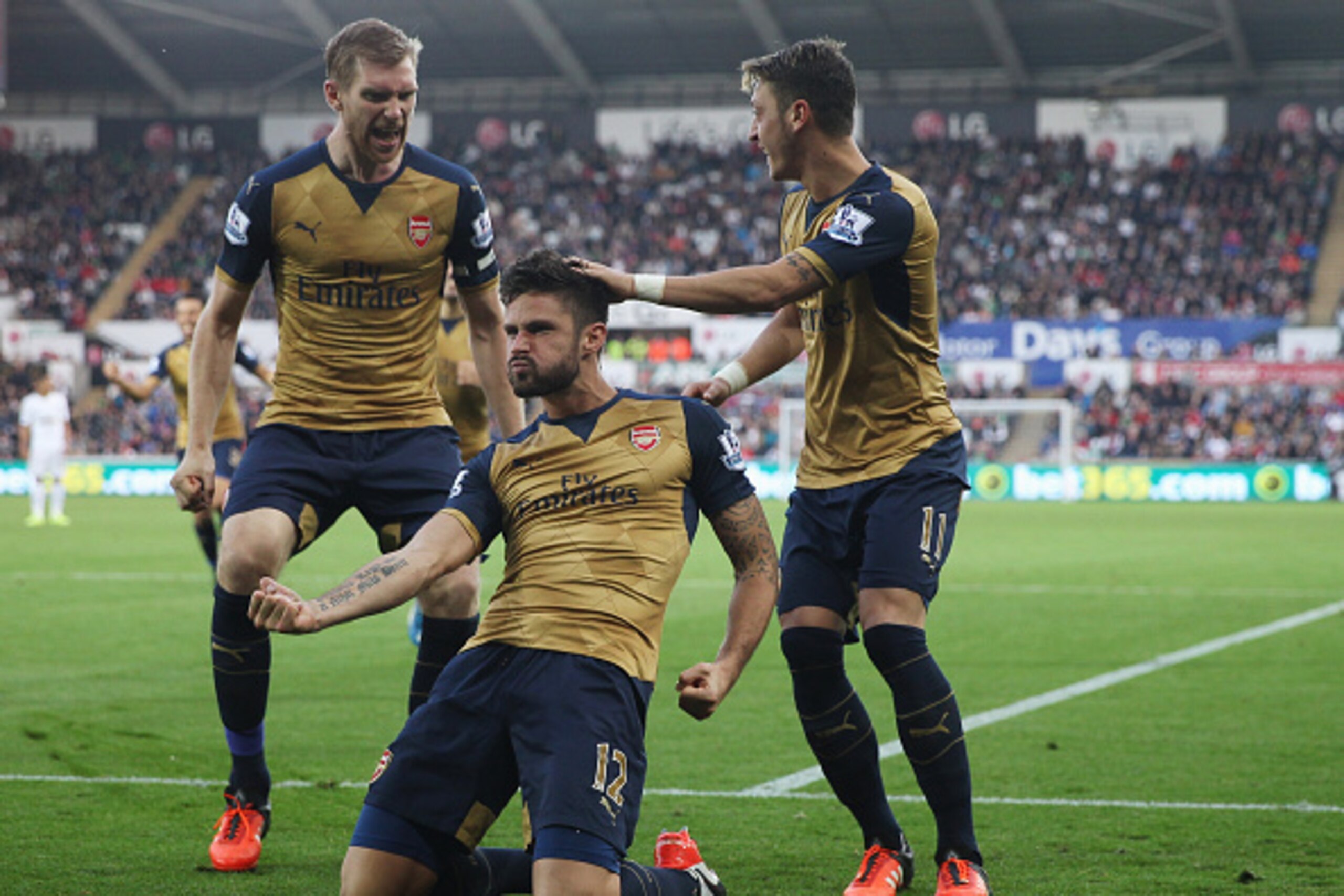 SWANSEA, WALES - OCTOBER 31: Olivier Giroud (C) of Arsenal celebrates scoring his team's first goal  with his team mates Per Mertesacker (L) and Mesut Ozil (R) during the Barclays Premier League match between Swansea City and Arsenal at Liberty Stadium on