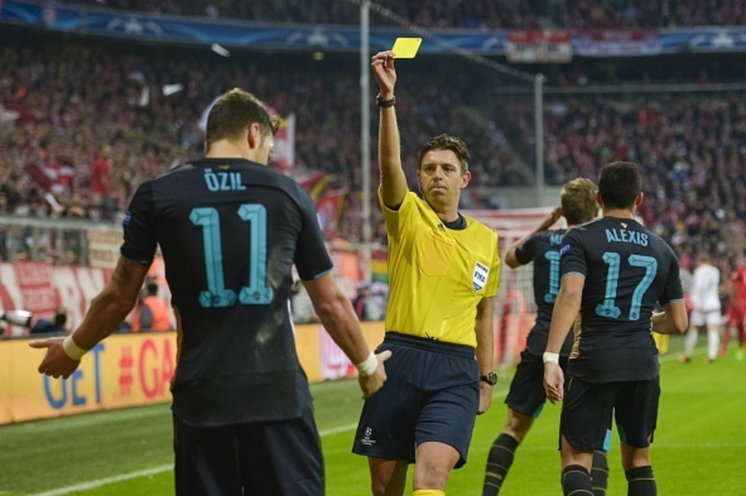 Italian Referee Gianluca Rocchi (C) shows Arsenal's German midfielder Mesut Oezil (L) the yellow card during the UEFA Champions League Group F second-leg football match between FC Bayern Munich and Arsenal FC in Munich, southern Germany, on November 4, 20