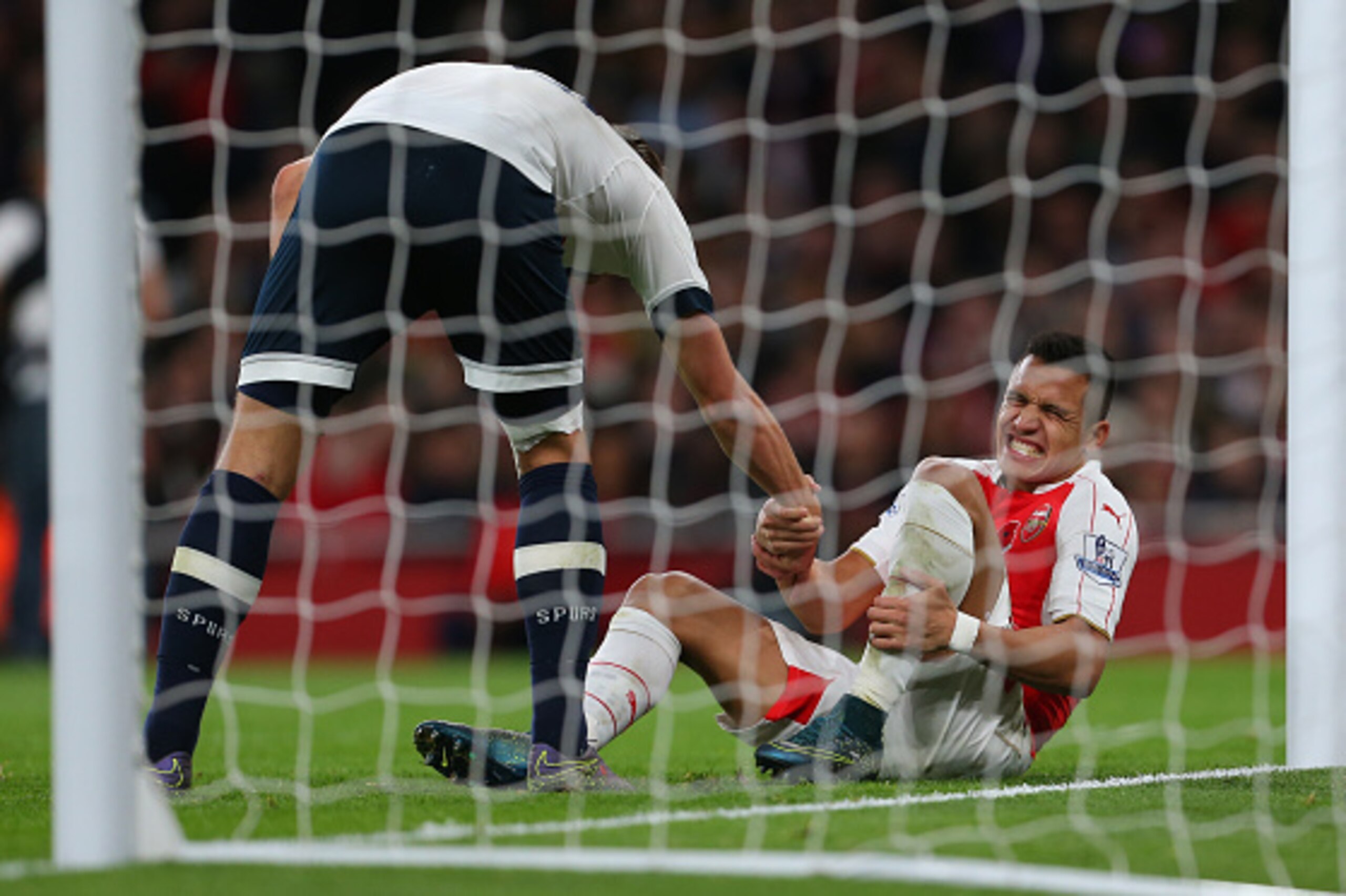 LONDON, ENGLAND - NOVEMBER 08:  Alexis Sanchez of Arsenal grimaces as he is helped up during the Barclays Premier League match between Arsenal and Tottenham Hotspur at Emirates Stadium on November 8, 2015 in London, England.  (Photo by Catherine Ivill - A
