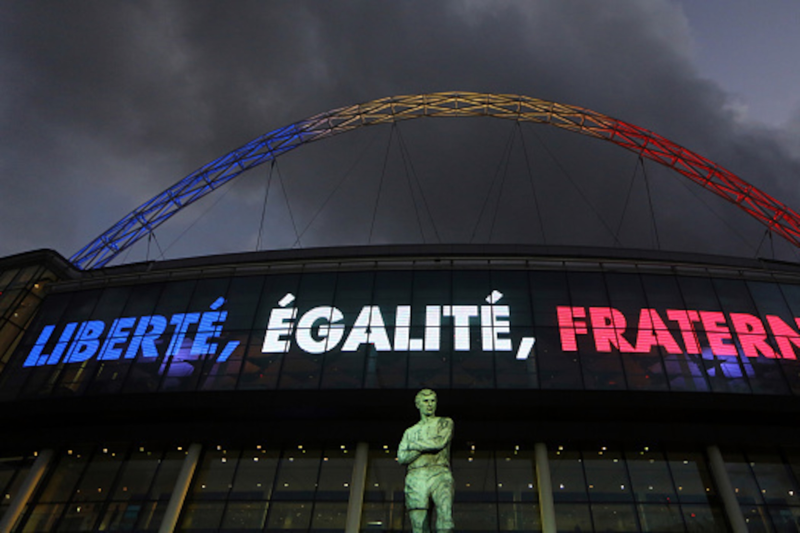 WEMBLEY, ENGLAND - NOVEMBER 17:  The Bobby Moore statue at Wembley stadium with the arch lit up in red, white and blue  of the French tricolour flag before the international friendly between England and France at Wembley Stadium on November 17, 2015 in Lo