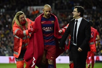 Barcelona's Argentinian defender Javier Mascherano (C) walks with a blanket around him assisted by a medic during the Spanish league 'Clasico' football match Real Madrid CF vs FC Barcelona at the Santiago Bernabeu stadium in Madrid on November 21, 2014.  