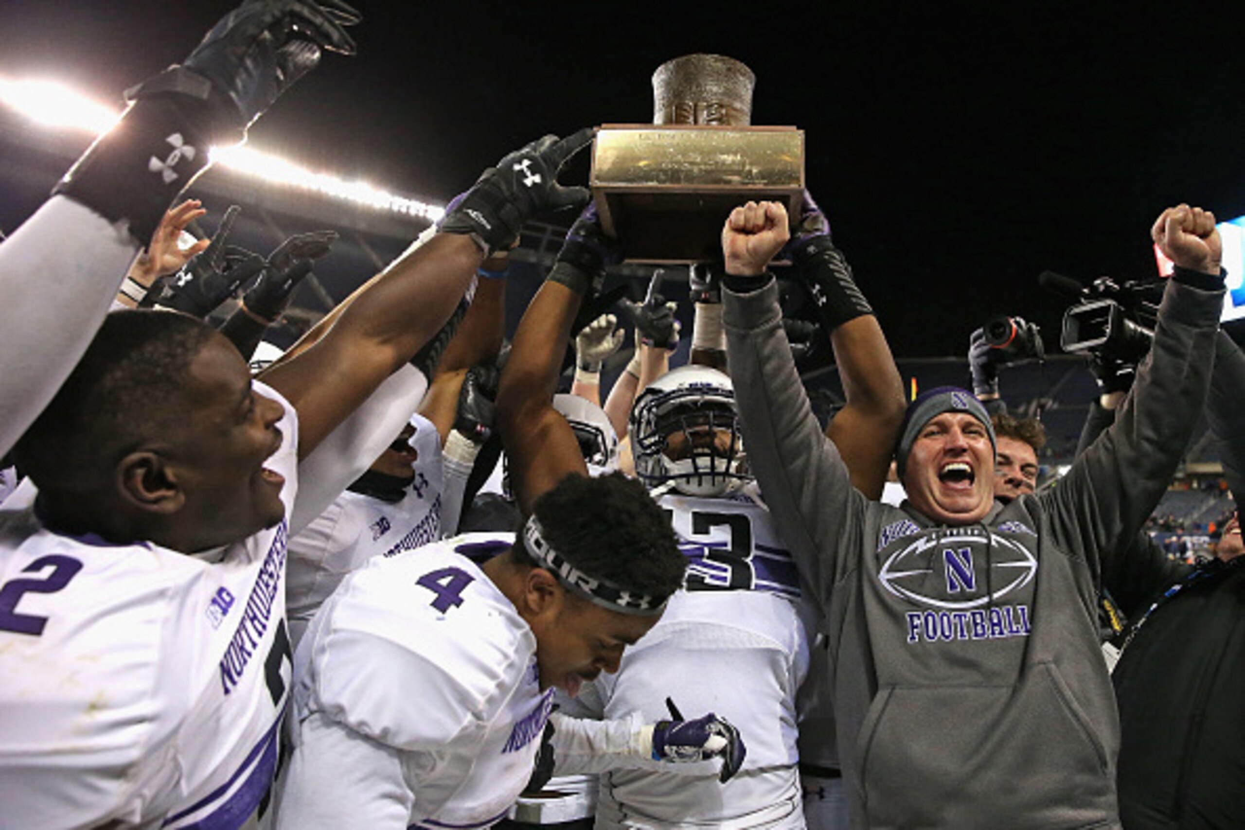 CHICAGO, IL - NOVEMBER 28:  Head coach Pat Fitzgerald of the Northwestern Wildcats (R) celebrates with his team including (L-R) Traveon Henry #2, Solomon Vault #4 and Deonte Gibson #13  as they hold the 'Land of Lincoln' trophy after a win over the Illino