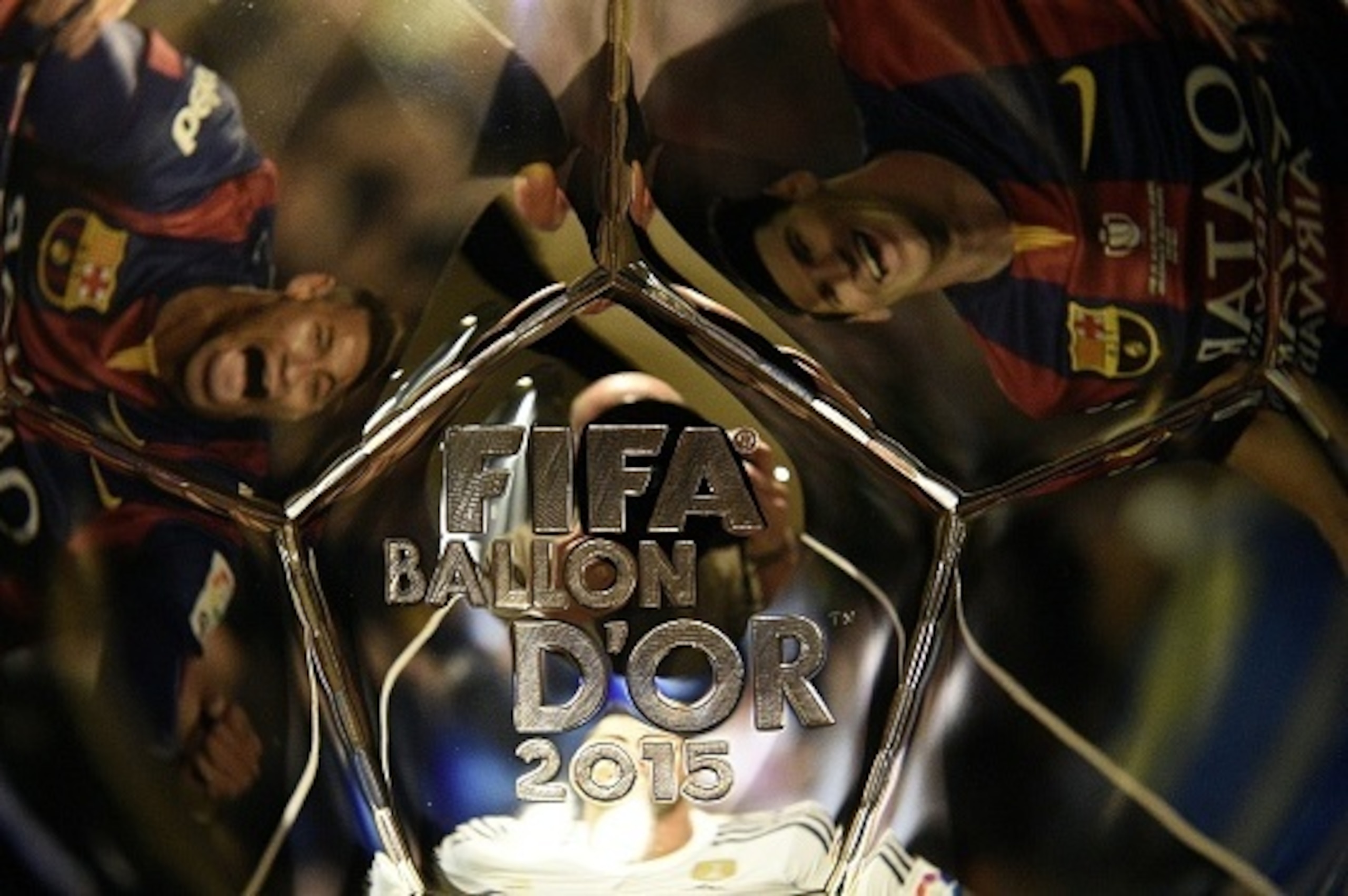 A picture taken on December 15, 2015 shows (From L) images of Barcelona's Brazilian forward Neymar, Real Madrid's Portuguese forward Cristiano Ronaldo and  Barcelona's Argentinian forward Lionel Messi, reflecting into the Ballon d'Or 2015 trophy displayed