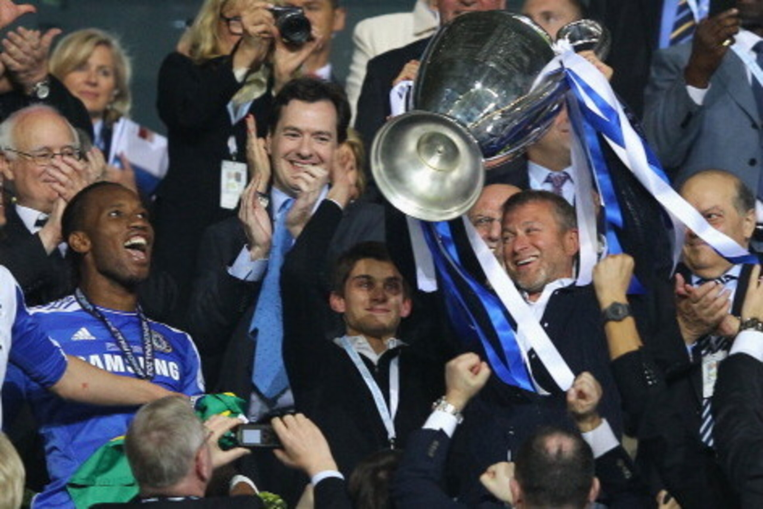 MUNICH, GERMANY - MAY 19: Club owner Roman Abramovich (R) lifts the trophy in celebration while Chancellor of the Exchequer George Osborne (C) applauds after their victory in the UEFA Champions League Final between FC Bayern Muenchen and Chelsea at the MUNICH, GERMANY - MAY 19: Club owner Roman Abramovich (R) lifts the trophy in celebration while Chancellor of the Exchequer George Osborne (C) applauds after their victory in the UEFA Champions League Final between FC Bayern Muenchen and Chelsea at the