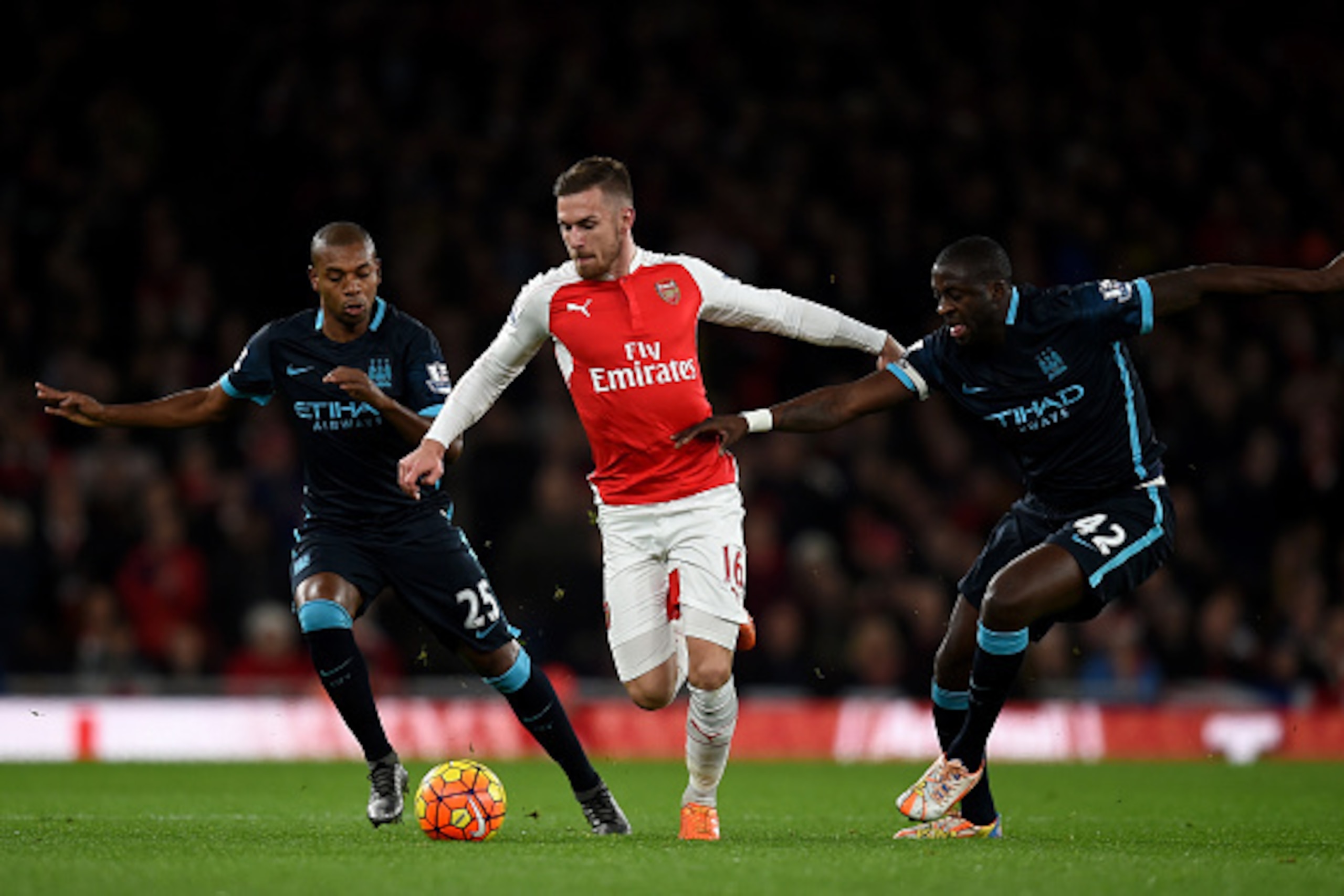 LONDON, ENGLAND - DECEMBER 21:  Aaron Ramsey of Arsenal (c) holds off Fernandinho of Manchester City (L) and Yaya Toure of Manchester City during the Barclays Premier League match between Arsenal and Manchester City at Emirates Stadium on December 21, 201