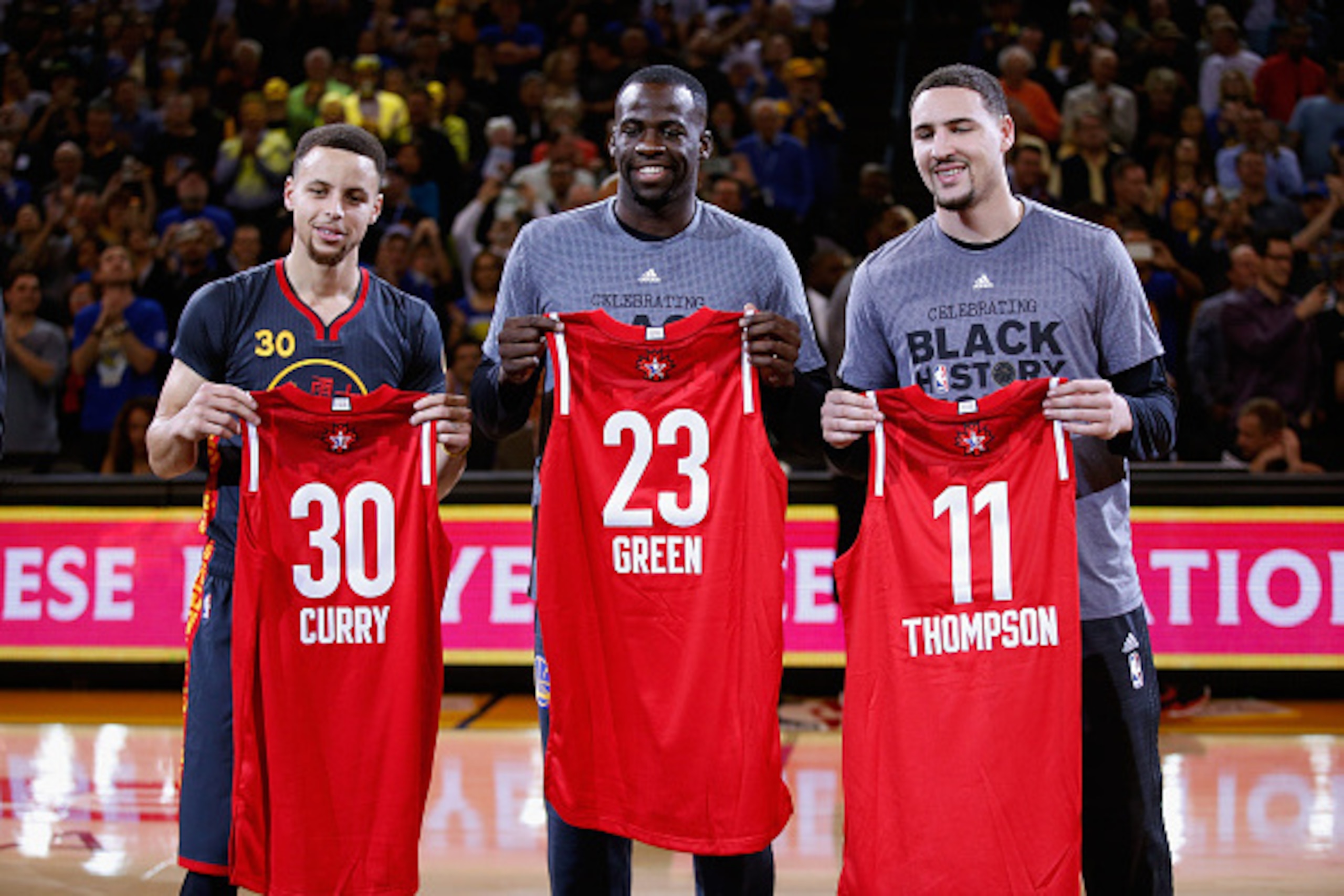 OAKLAND, CA - FEBRUARY 09:  (L-R) Stephen Curry #30, Draymond Green #23 and Klay Thompson #11 of the Golden State Warriors hold up their respective All-Star jerseys before their game against the Houston Rockets at ORACLE Arena on February 9, 2016 in Oakla