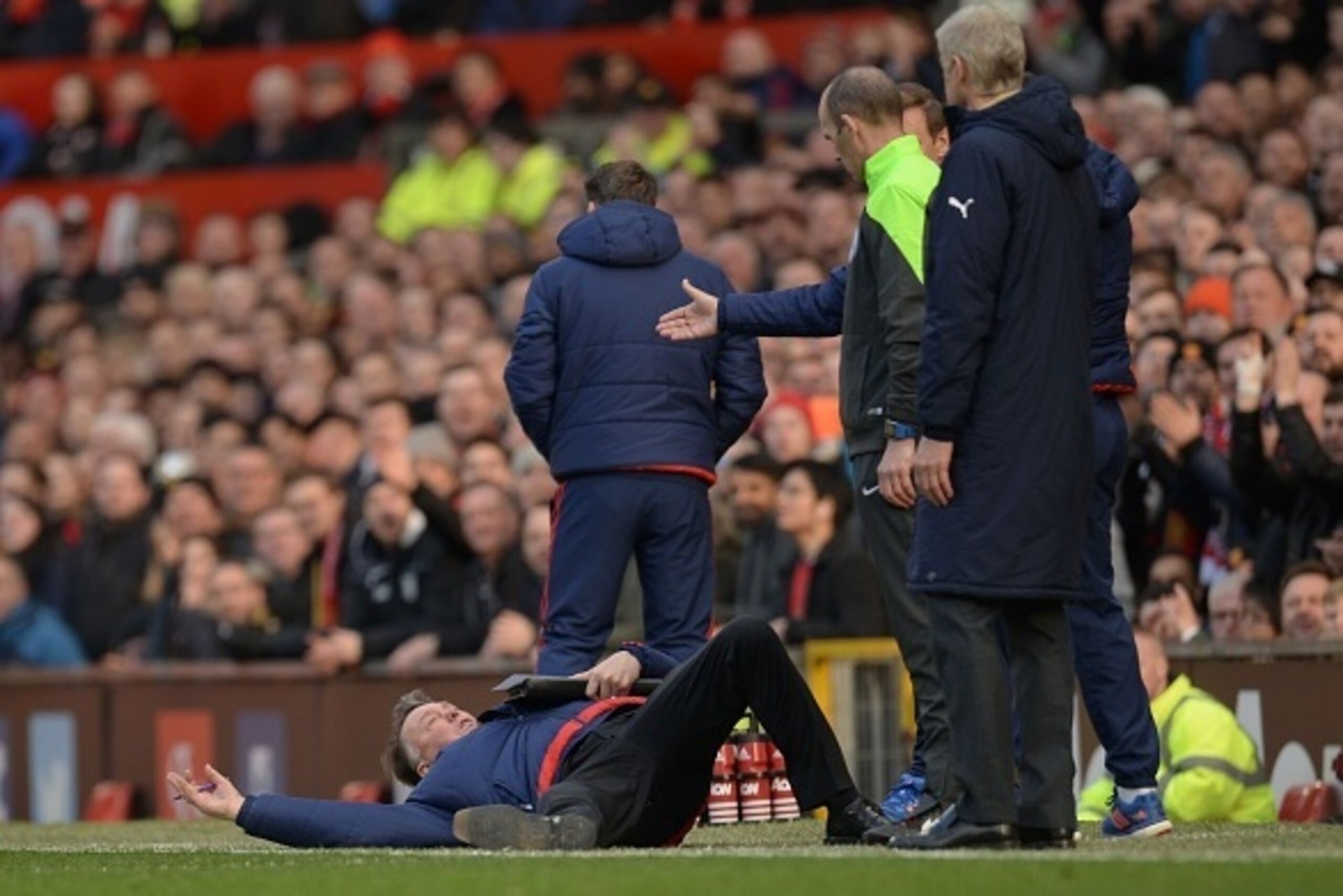 Manchester United's Dutch manager Louis van Gaal (L) falls over on the touchline in front of fourth official Mike Dean (2R) and Arsenal's French manager Arsene Wenger (R) during the English Premier League football match between Manchester United and Arsen