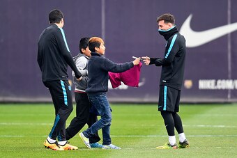 BARCELONA, SPAIN - MARCH 15:  Lionel Messi of FC Barcelona signs his autograph for youkng fans who ran onto the training pitch during a Barcelona training session ahead of the UEFA Champions League round of 16 second leg match between Barcelona and Arsena