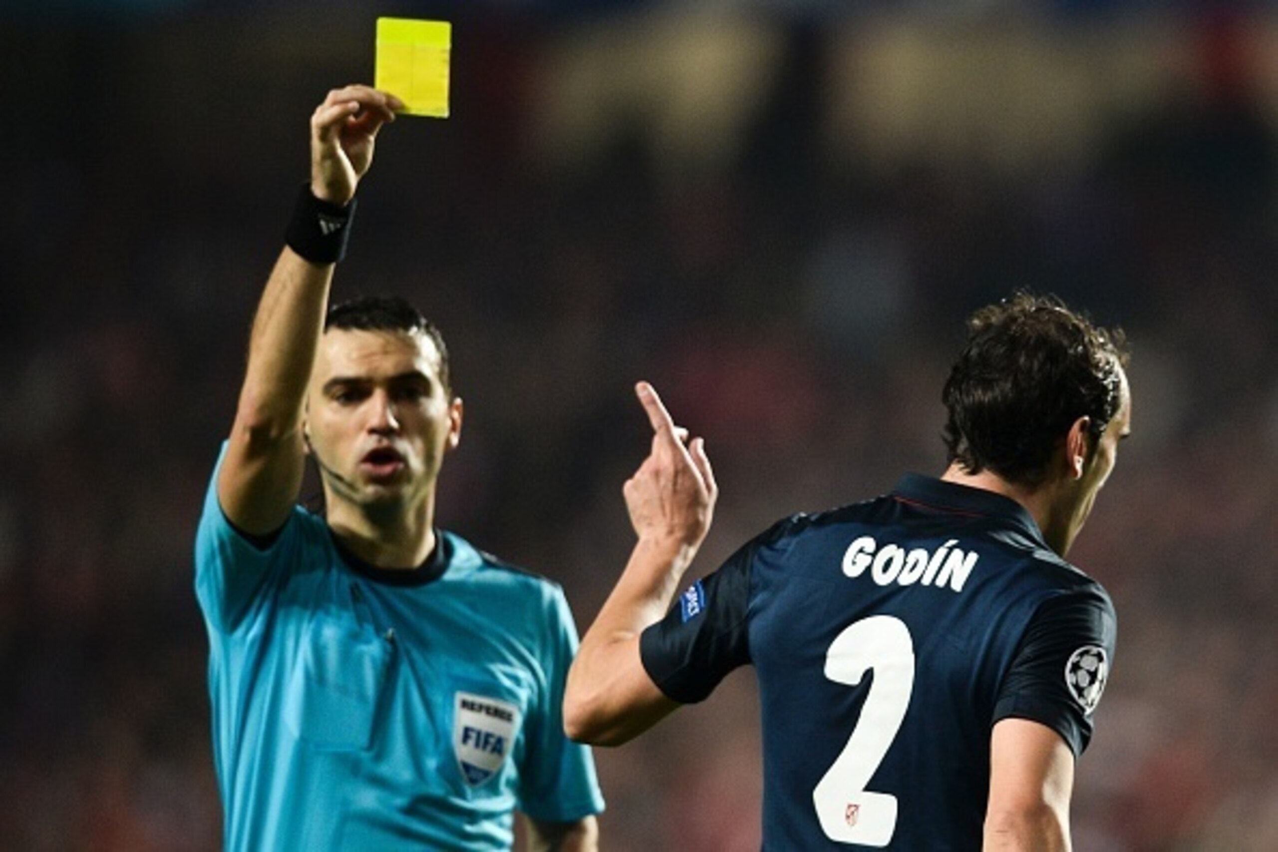 TOPSHOT - Atletico Madrid's Uruguayan defender Diego Godin (R) is shown a yellow card from referee Ovidiu Hategan (L) during the UEFA Champions League Group C football match SL Benfica vs Club Atletico de Madrid at the Luz stadium in Lisbon on December 8,