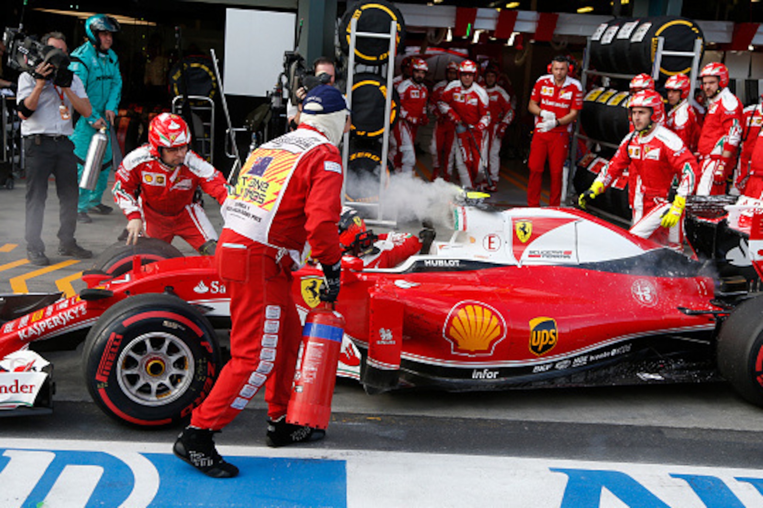 Ferrari's Finnish driver Kimi Raikkonen (L) climbs out of his car as a fire in the car is extinguished in the pit lane during the Formula One Australian Grand Prix in Melbourne on March 20,  2016. / AFP / POOL / BRANDON MALONE / IMAGE STRICTLY RESTRICTED 