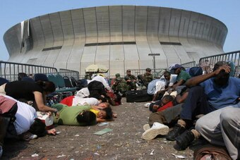 New Orleans, UNITED STATES:  (FILES): This 03 September 2005 file photo shows people waiting to be evacuated from the Superdome (BACKGROUND) in New Orleans taking cover after the National Guard reported shots being fired outide the arena, six days after H