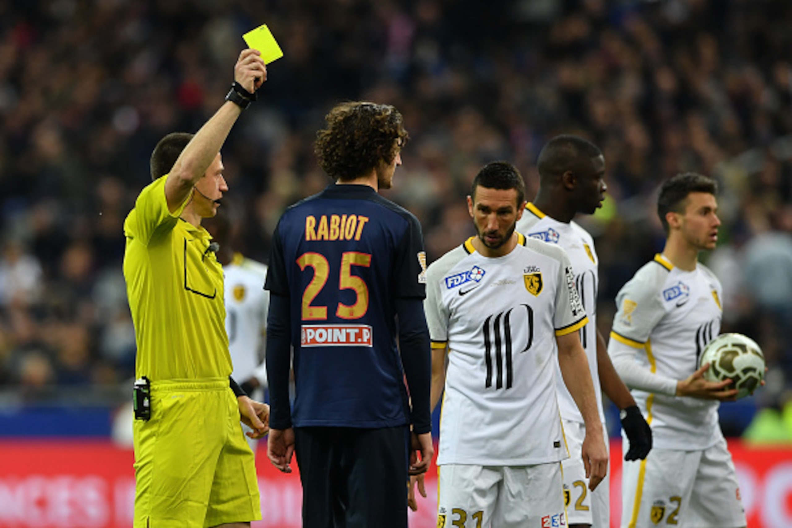 French referee Ruddy Buquet (L) gives a yellow card to Paris Saint-Germain's French midfielder Adrien Rabiot (C) during the French League Cup final football match between Paris Saint-Germain and Lille on April 23, 2016 at the Stade de France in Saint-Deni