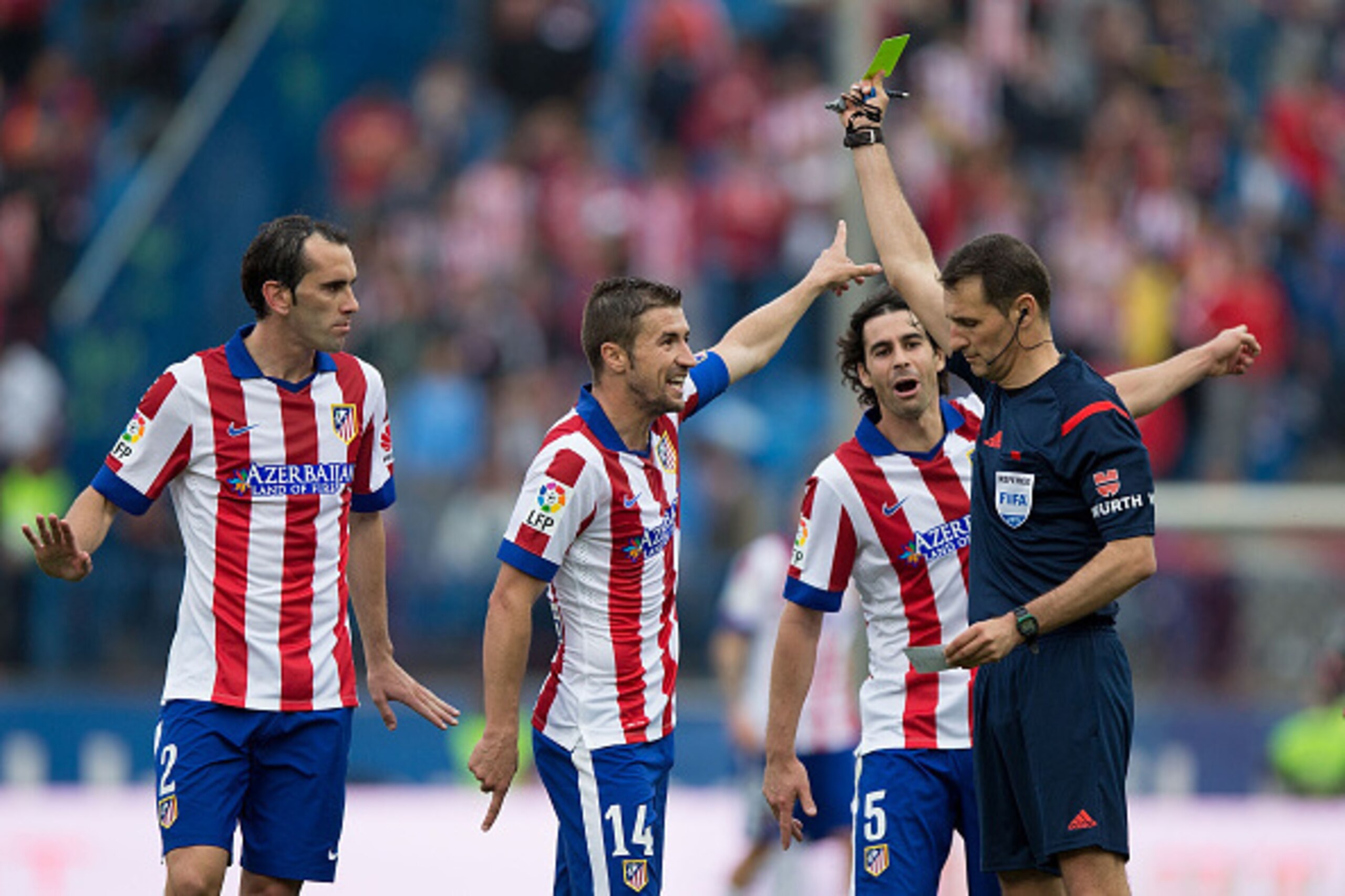 MADRID, SPAIN - APRIL 25: referee Clos Gomez (R) shiws the yellow card to Gabi Fernandez (2ndL) as his teammates Diego Godin (L) and Tiago Mendes (2ndR) protest during the La Liga match between Club Atletico de Madrid and Elche FC at Vicente Calderon Stad
