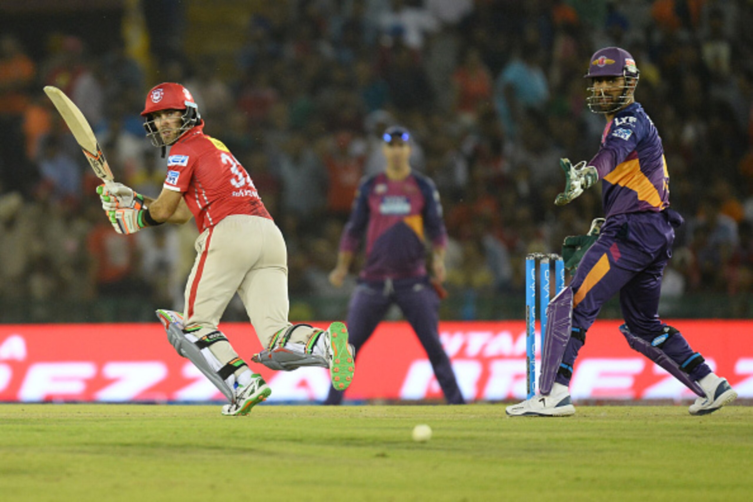 Kings XI Punjab  Glenn Maxwell (L) plays a shot as Rising Pune Supergiants captain Mahendra Singh Dhoni  looks on during the 2016 Indian Premier League (IPL) Twenty20 cricket match between Rising Pune Supergiants and Kings XI Punjab at The Punjab Cricket 