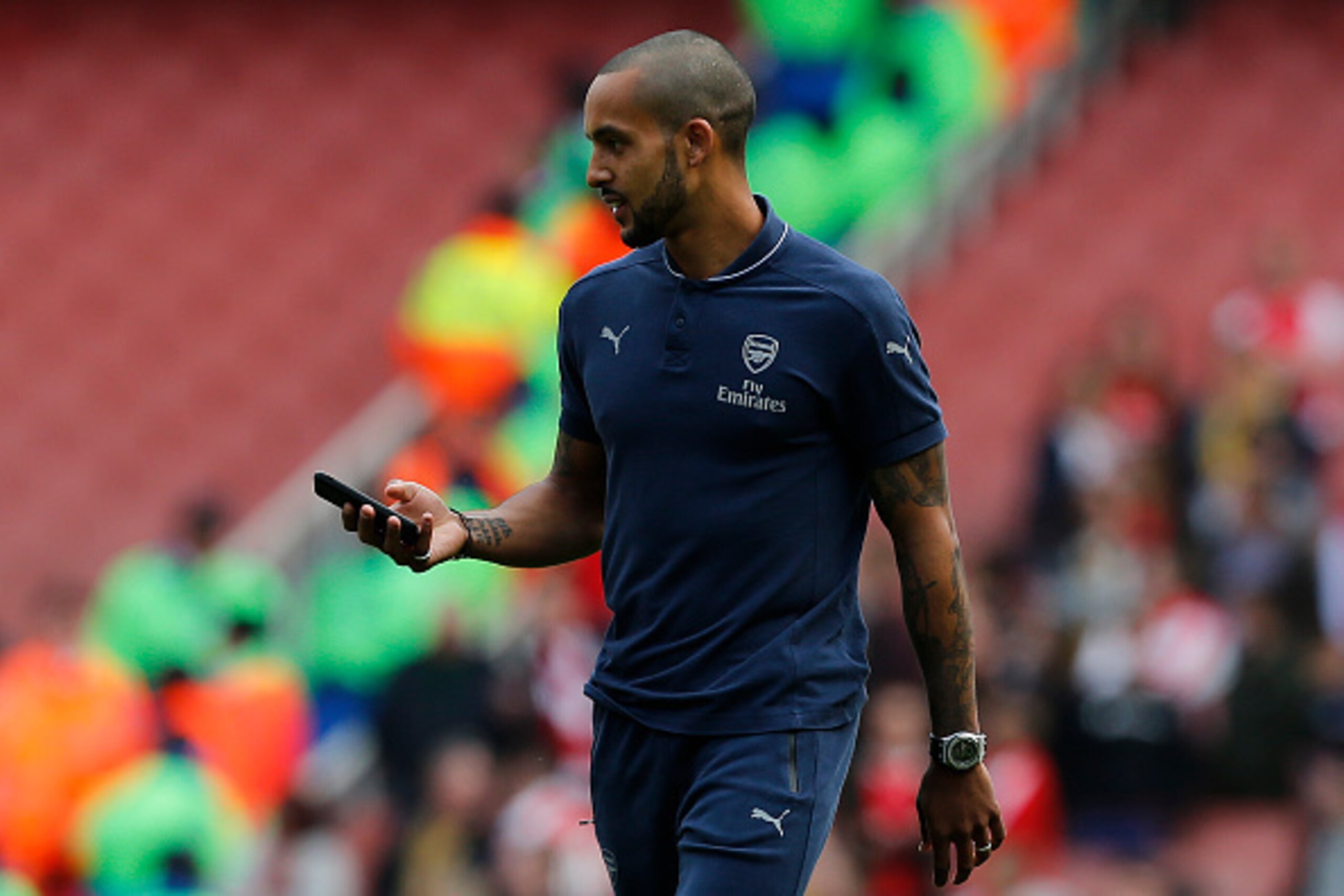 Arsenal's English midfielder Theo Walcott carrys a mobile phone as he walks around the pitch following the English Premier League football match between Arsenal and Aston Villa at the Emirates Stadium in London on May 15, 2016.  / AFP / Ian Kington / REST