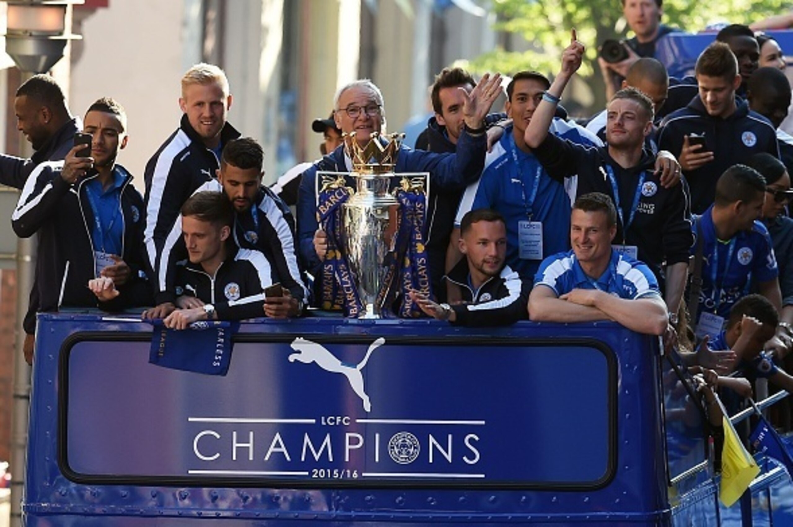 Leicester City's Italian manager Claudio Ranieri (C) holds the Premier league trophy as Leicester City's English striker Jamie Vardy raises his arms (R) to fans as the Leicester City team take part in an open-top bus parade through Leicester to celebrate 
