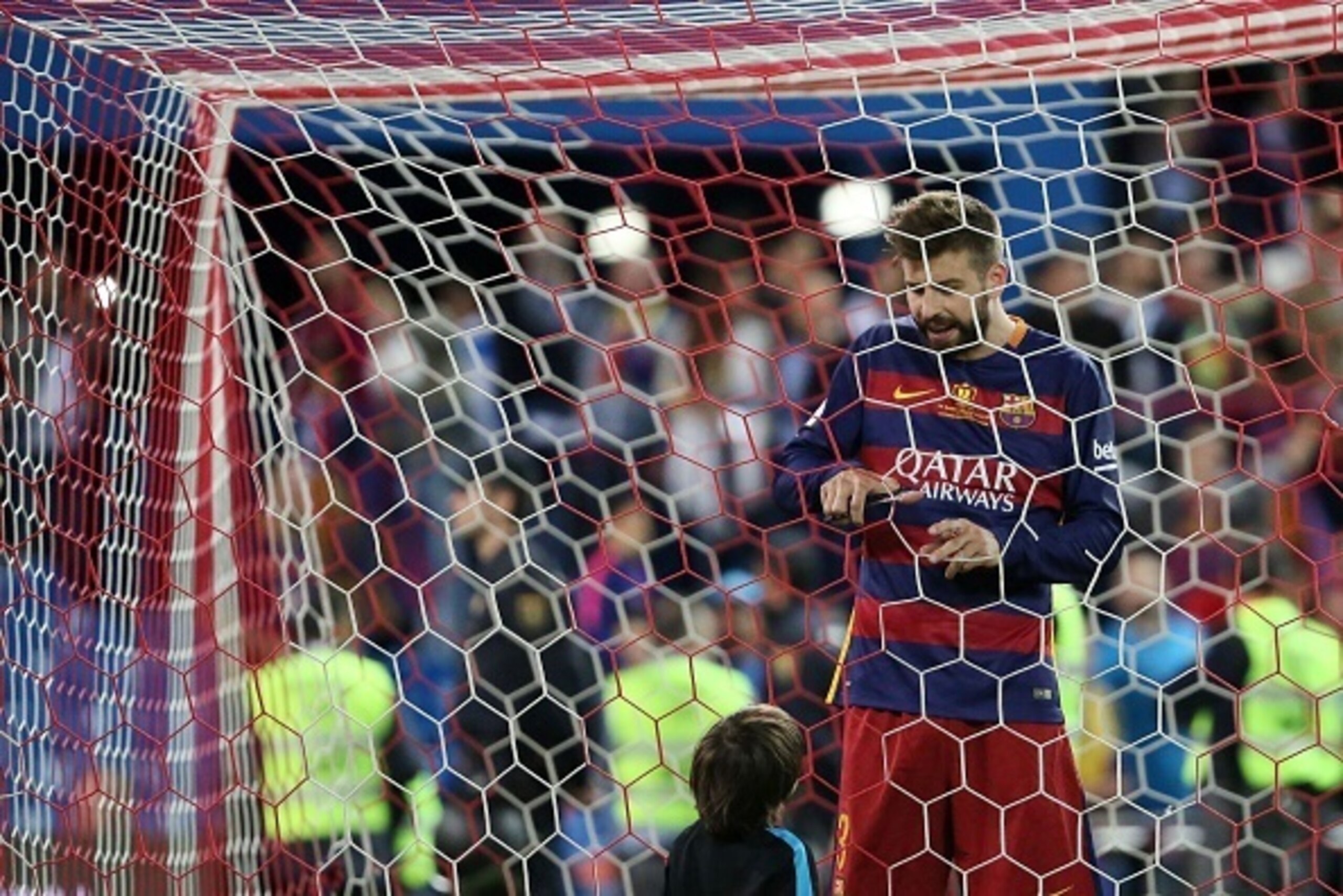 Barcelona's defender Gerard Pique (R) cuts the net of the goal as Messi's son looks at him after winning the Spanish 'Copa del Rey' (King's Cup) final match FC Barcelona vs Sevilla FC at the Vicente Calderon stadium in Madrid on May 22, 2016. / AFP / CESA