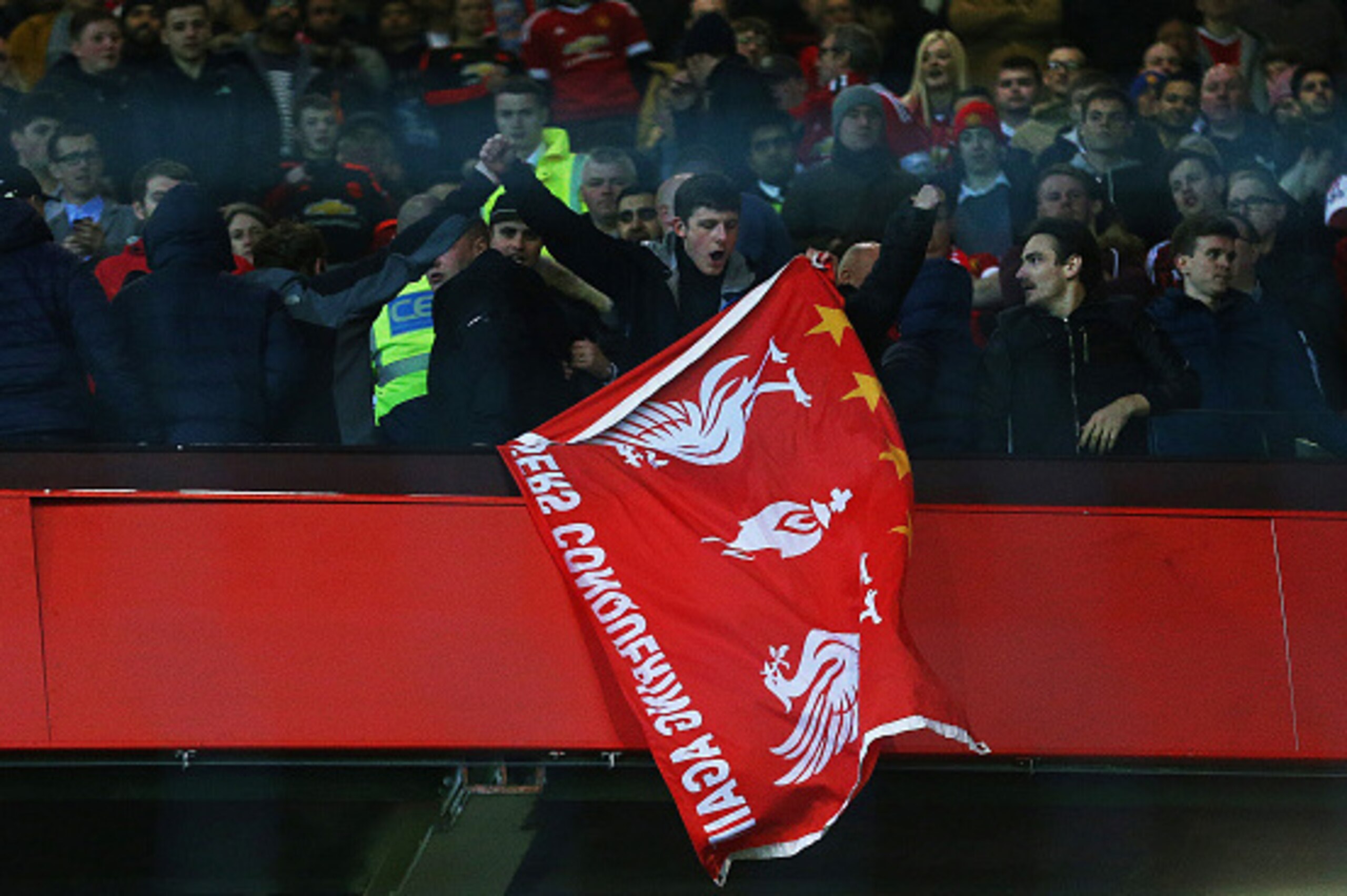 MANCHESTER, ENGLAND - MARCH 17:  A Liverpool fan holds a flag as he stands amongst Manchester United supporters after the UEFA Europa League round of 16, second leg match between Manchester United and Liverpool at Old Trafford on March 17, 2016 in Manches
