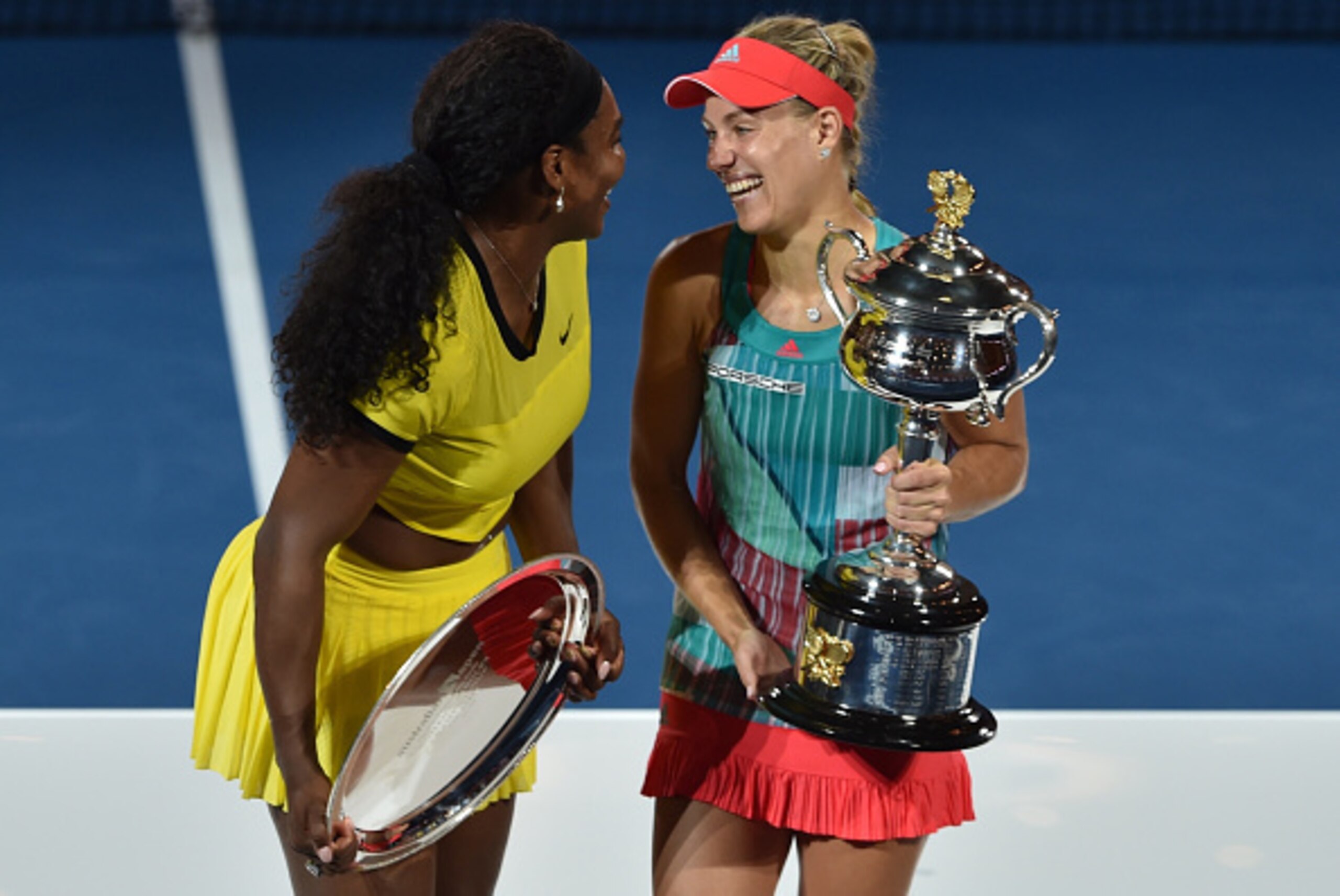 Angelique Kerber of Germany (R) shares a laugh with Serena Williams of the US (L) as she holds the winner's trophy during the awards ceremony after their women's singles final match on day 13 of the 2016 Australian Open tennis tournament in Melbourne on J