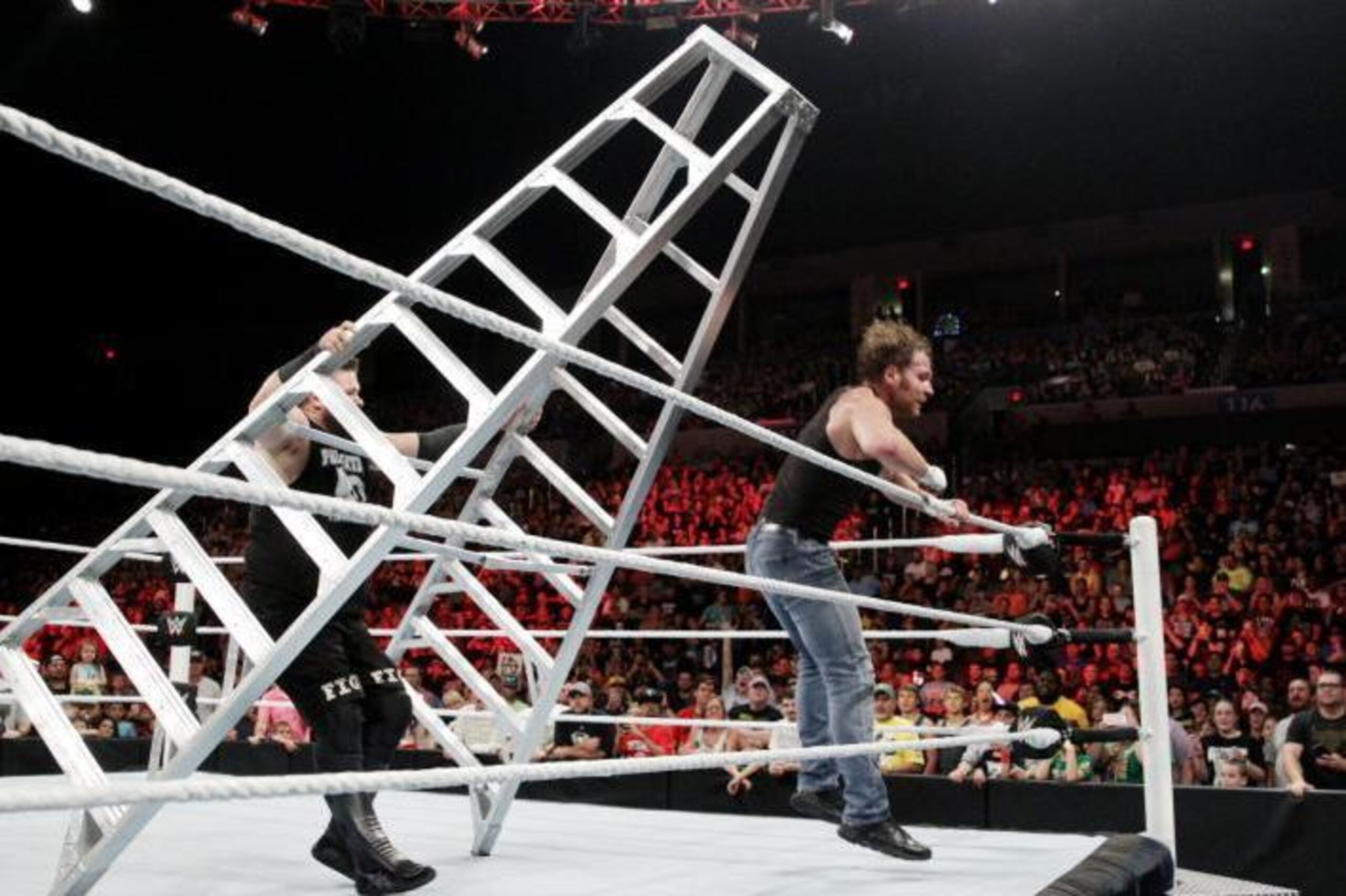 Kevin Owens pushes Dean Ambrose off a ladder.