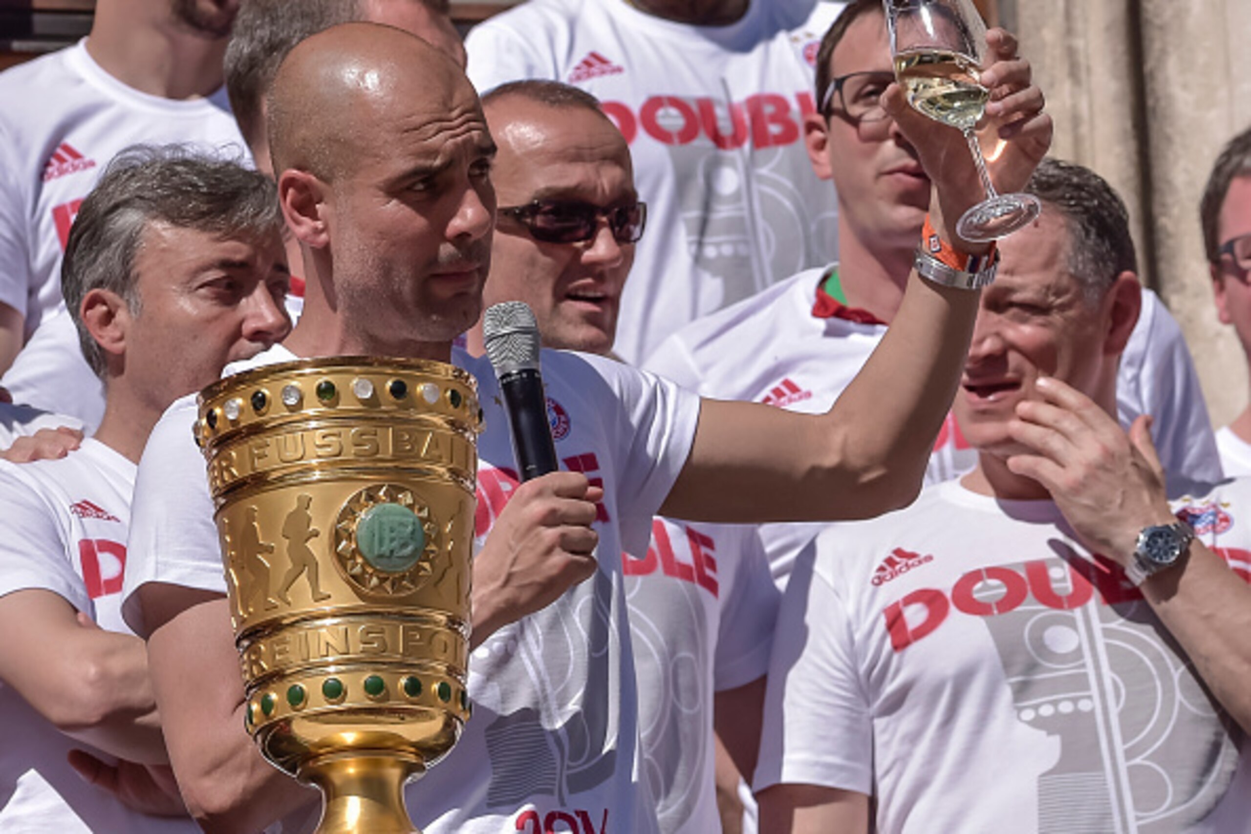 Bayern Munich's Spanish head coach Pep Guardiola stands behind the German Cup trophy on the balcony of Munich's city hall as Bayern Munich's team members celebrate with their fans winning the trophies of the German Cup and the German League during a FC Ba Bayern Munich's Spanish head coach Pep Guardiola stands behind the German Cup trophy on the balcony of Munich's city hall as Bayern Munich's team members celebrate with their fans winning the trophies of the German Cup and the German League during a FC Ba
