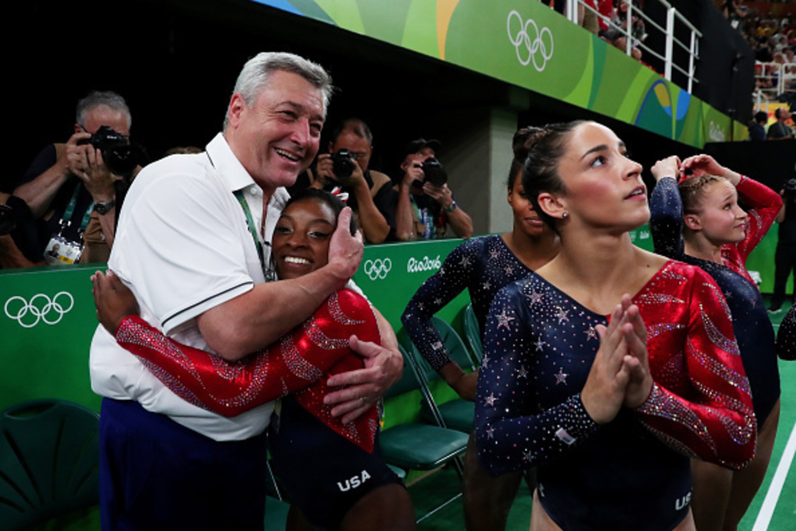 RIO DE JANEIRO, BRAZIL - AUGUST 07: Simone Biles (2nd L) of the United States is embraced by coach Mihai Brestyan (1st L) after Women's qualification for Artistic Gymnastics on Day 2 of the Rio 2016 Olympic Games at the Rio Olympic Arena on August 7, 2016