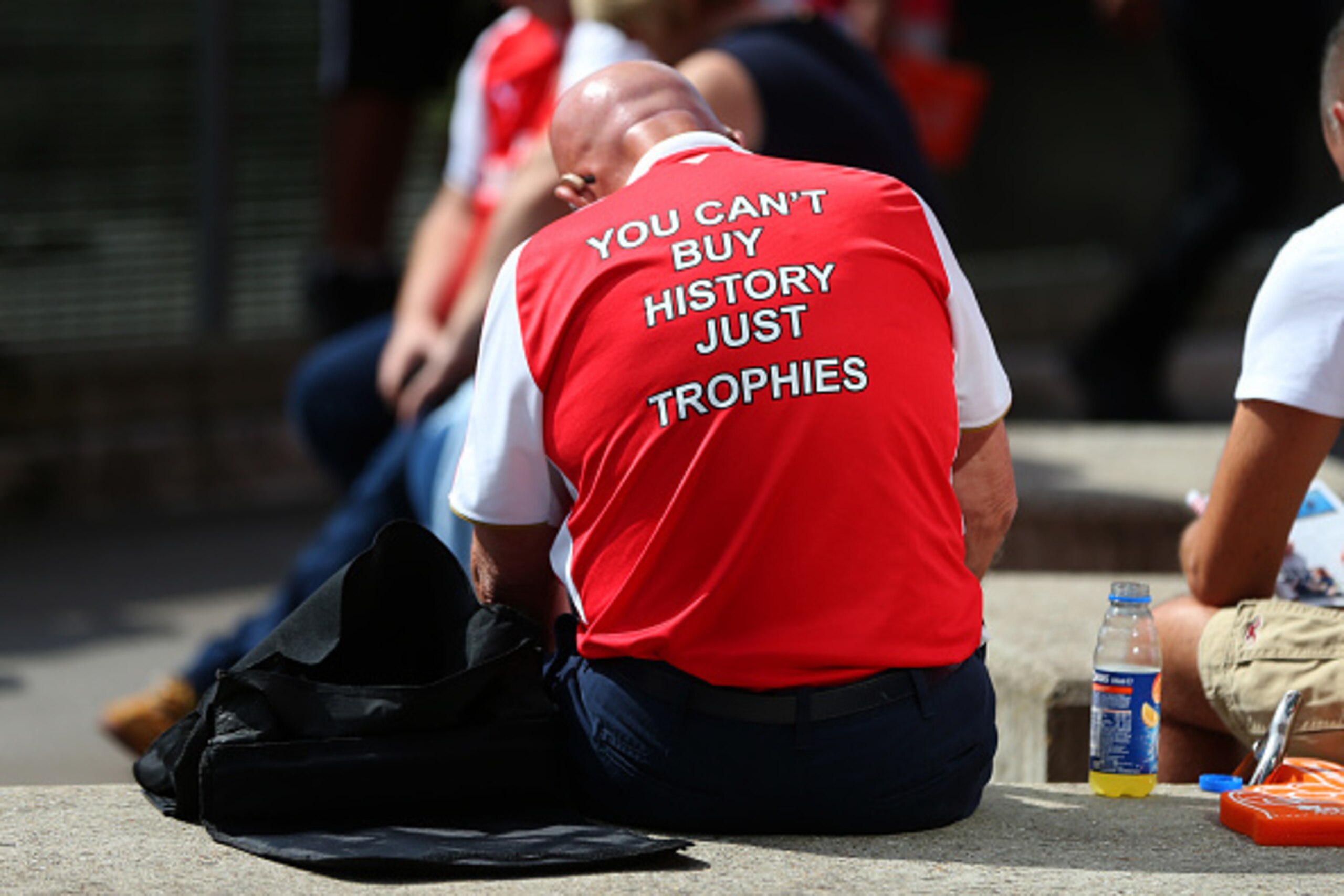 LONDON, ENGLAND - AUGUST 14: An Arsenal fan wears a shirt saying 'you can't buy history just trophies' before the Premier League match between Arsenal and Liverpool at Emirates Stadium on August 14, 2016 in London, England. (Photo by Catherine Ivill - AMA LONDON, ENGLAND - AUGUST 14: An Arsenal fan wears a shirt saying 'you can't buy history just trophies' before the Premier League match between Arsenal and Liverpool at Emirates Stadium on August 14, 2016 in London, England. (Photo by Catherine Ivill - AMA