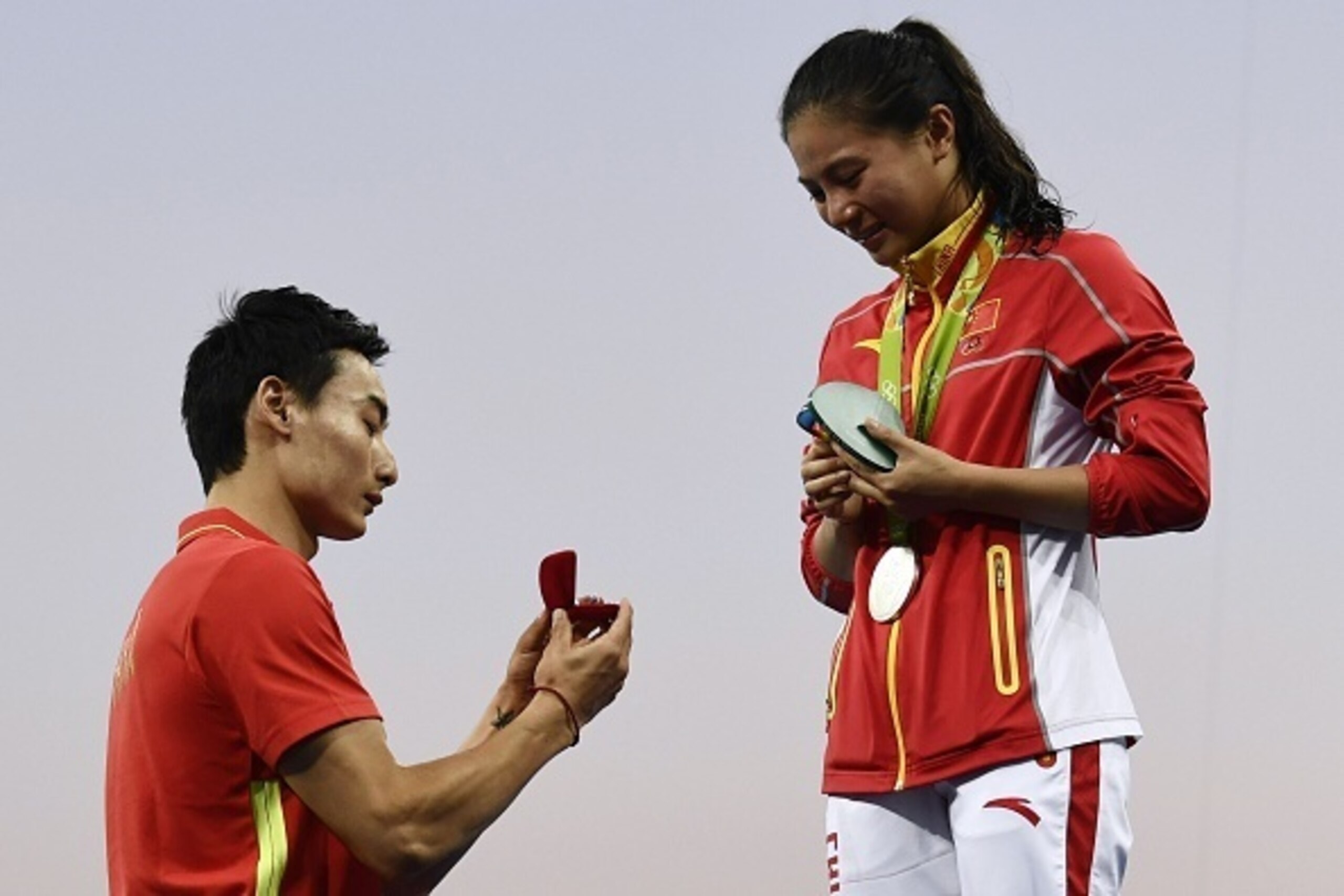 TOPSHOT - Silver medallist China's He Zi (R), reacts she receives a marriage proposal from Chinese diver Qin Kai during the podium ceremony of the Women's diving 3m Springboard Final at the Rio 2016 Olympic Games at the Maria Lenk Aquatics Stadium in Rio 