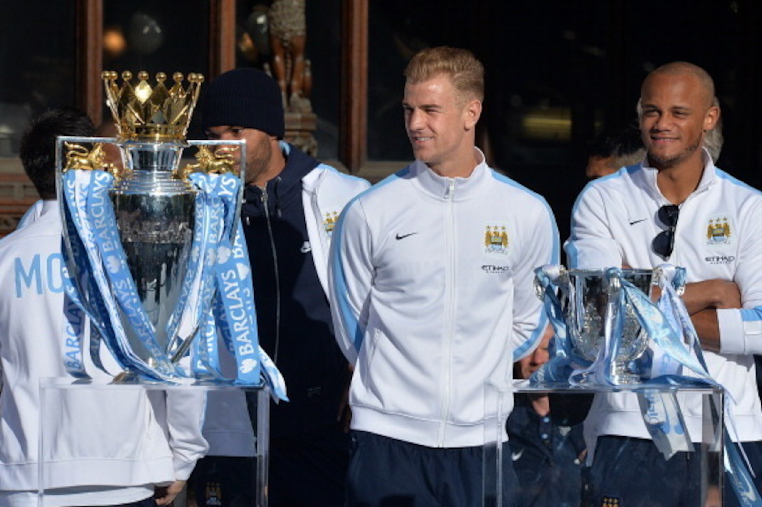 Manchester City's Belgian defender Vincent Kompany (R) and Manchester City's English goalkeeper Joe Hart (2nd R) stand beside the Premiership (L) and League Cup (R) trophies as they prepare to take part in a victory parade on an open-topped bus through th