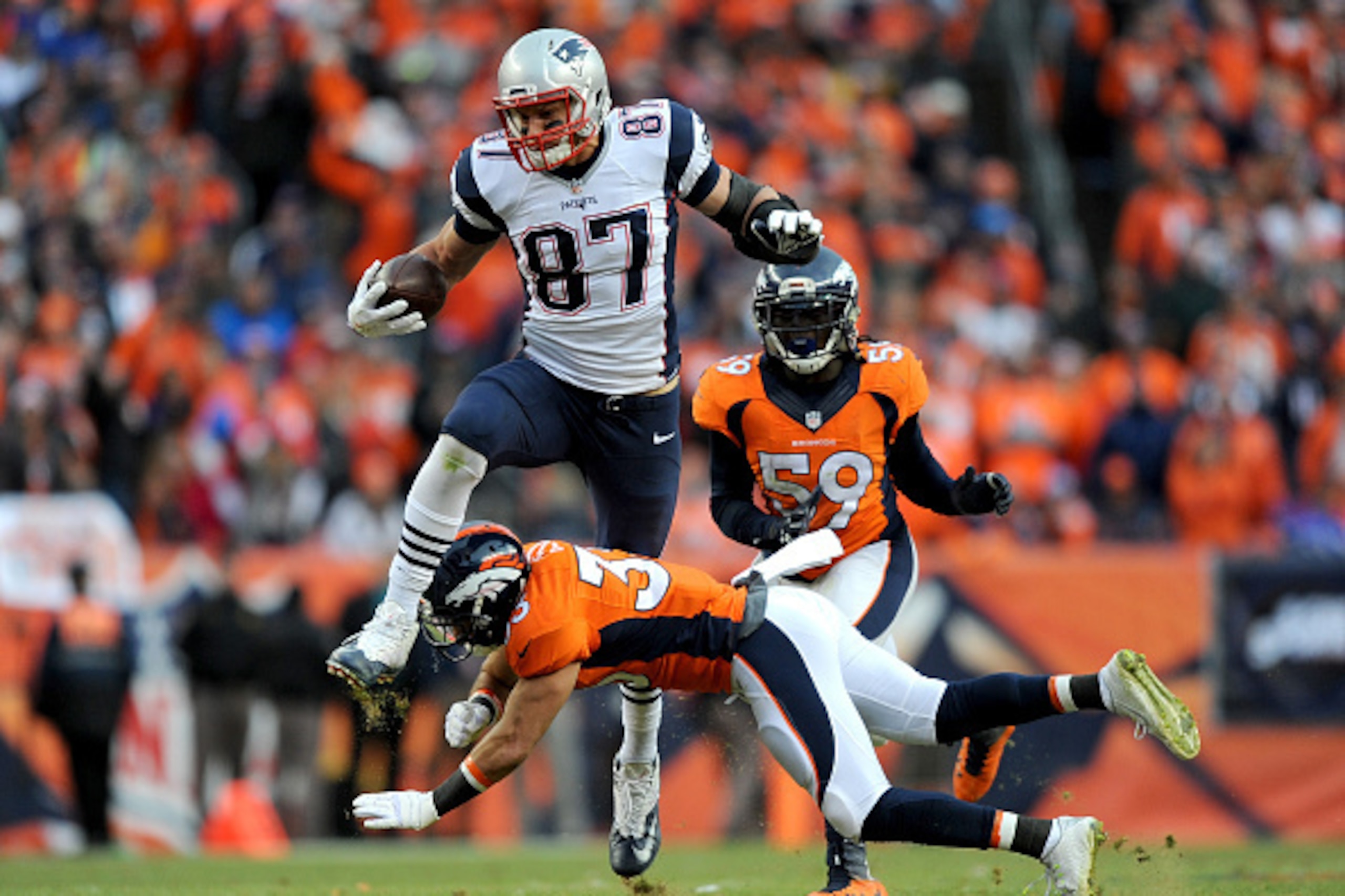 DENVER, CO - JANUARY 24:  Rob Gronkowski #87 of the New England Patriots is tackled by Shiloh Keo #33 and  Danny Trevathan #59 of the Denver Broncos in the fourth quarter in the AFC Championship game at Sports Authority Field at Mile High on January 24, 2
