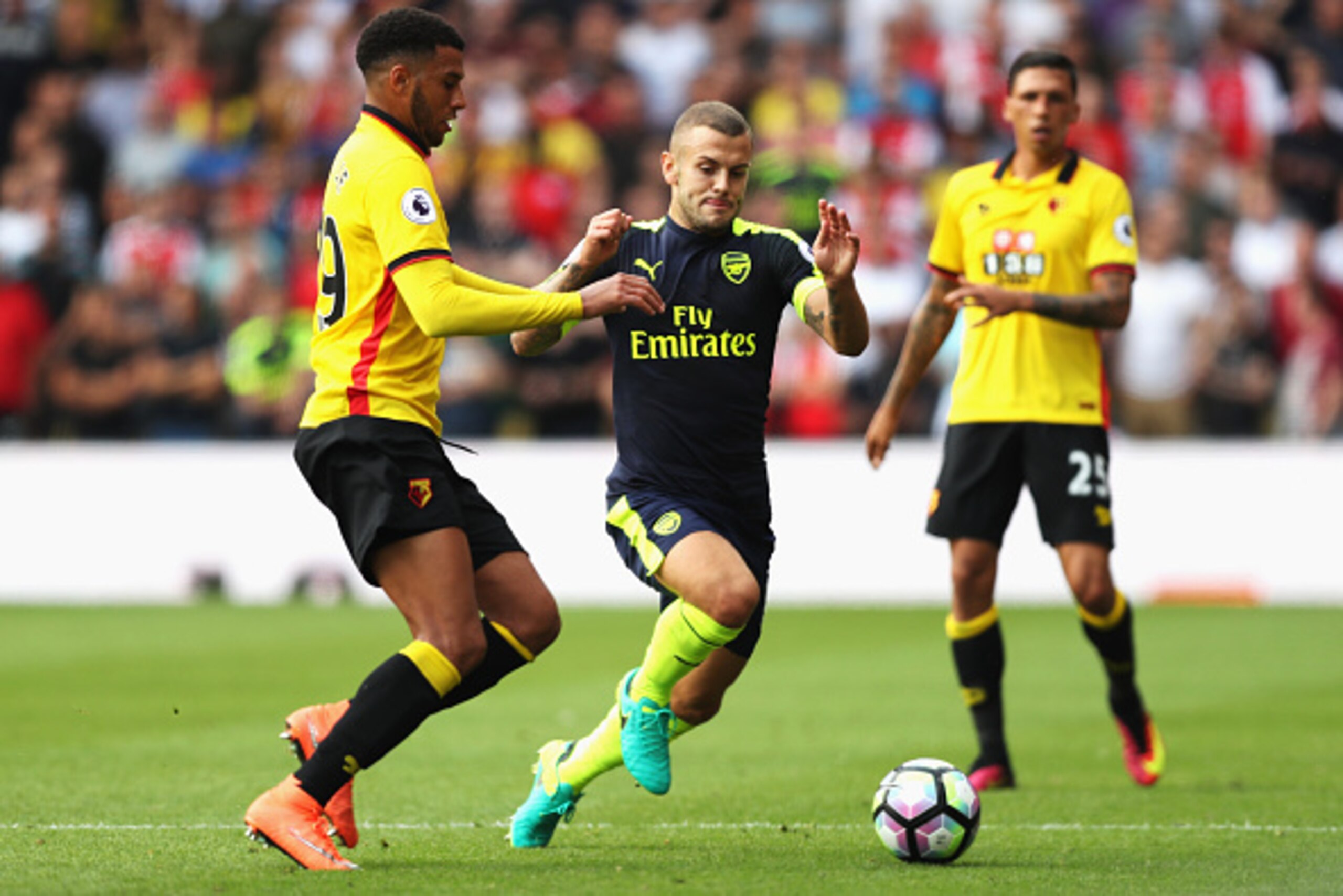 WATFORD, ENGLAND - AUGUST 27: Etienne Capoue of Watford (L) and Jack Wilshere of Arsenal (C) both challenge for the ball during the Premier League match between Watford and Arsenal at Vicarage Road on August 27, 2016 in Watford, England.  (Photo by Christ
