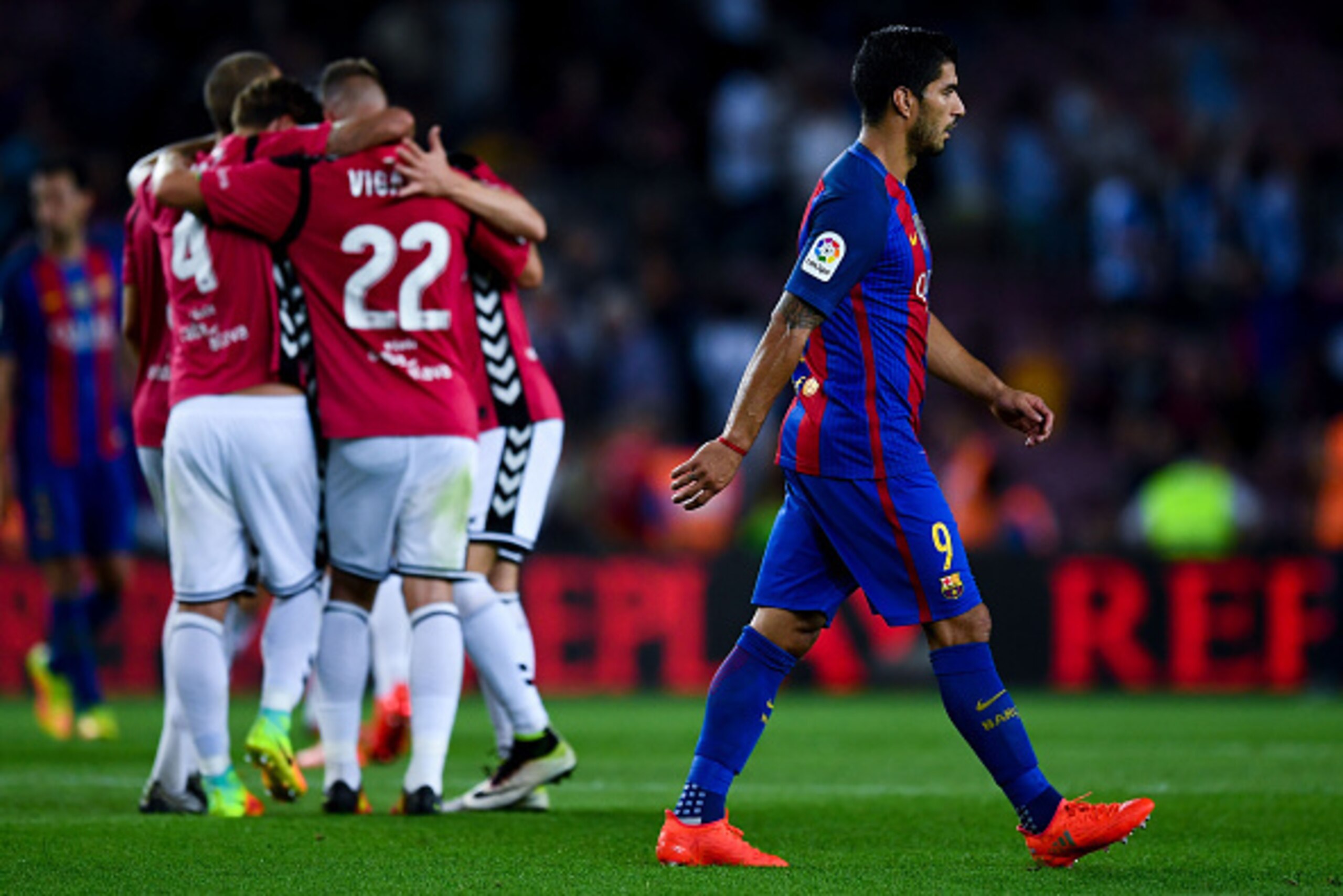BARCELONA, SPAIN - SEPTEMBER 10:  Luis Suarez of FC Barcelona leaves the pitch dejected as Deportivo Alaves players celebrate victory at the end of the La Liga match between FC Barcelona and Deportivo Alaves at Camp Nou stadium on September 10, 2016 in Ba