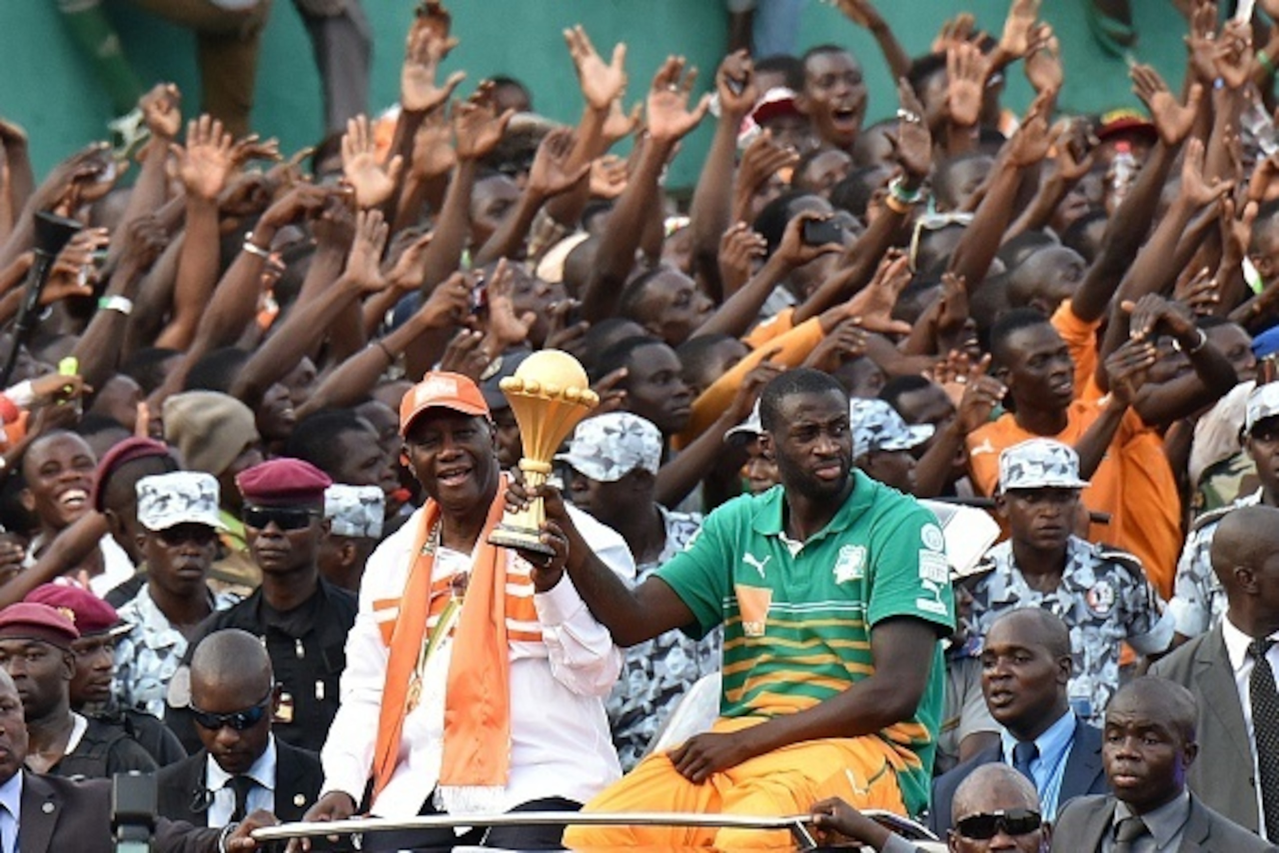 Ivorians celebrate as President Alassane Ouattara (C-L) and Ivory Coast's midfielder and captain Yaya Toure (C-R) hold the 2015 African Cup of Nations trophy during a welcoming parade in Abidjan on February 9, 2015. Ivory Coast ended a 23-year Africa Cup 