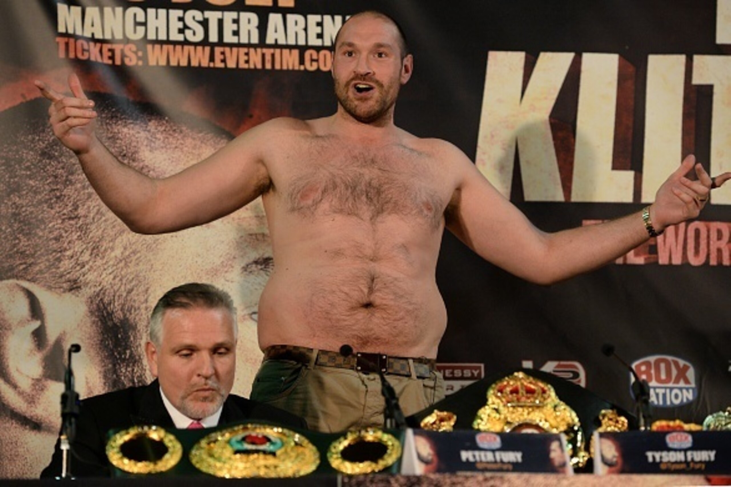British heavyweight boxer Tyson Fury (C) gestures after removing his t-shirt during a press conference to publicise his forthcoming world heavyweight title fight against Ukranian heavyweight Wladimir Klitschko, at the Manchester Arena in Manchester, north