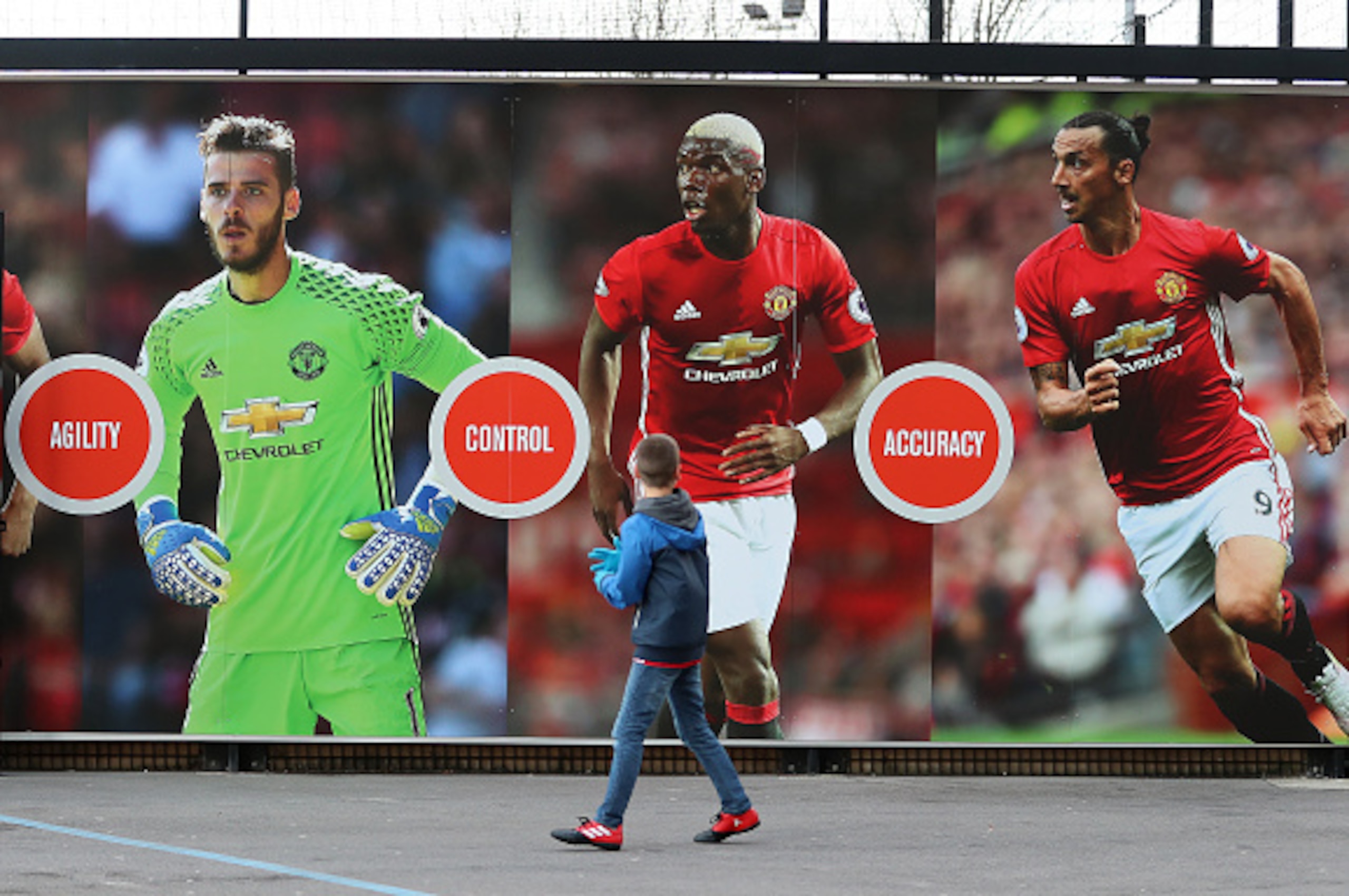 MANCHESTER, ENGLAND - DECEMBER 26: A young Manchester United supporter walks past a poster of Zlatan Ibrahimovic, Paul Pogba and David De Gea of Manchester United before the Premier League match between Manchester United and Sunderland at Old Trafford on 