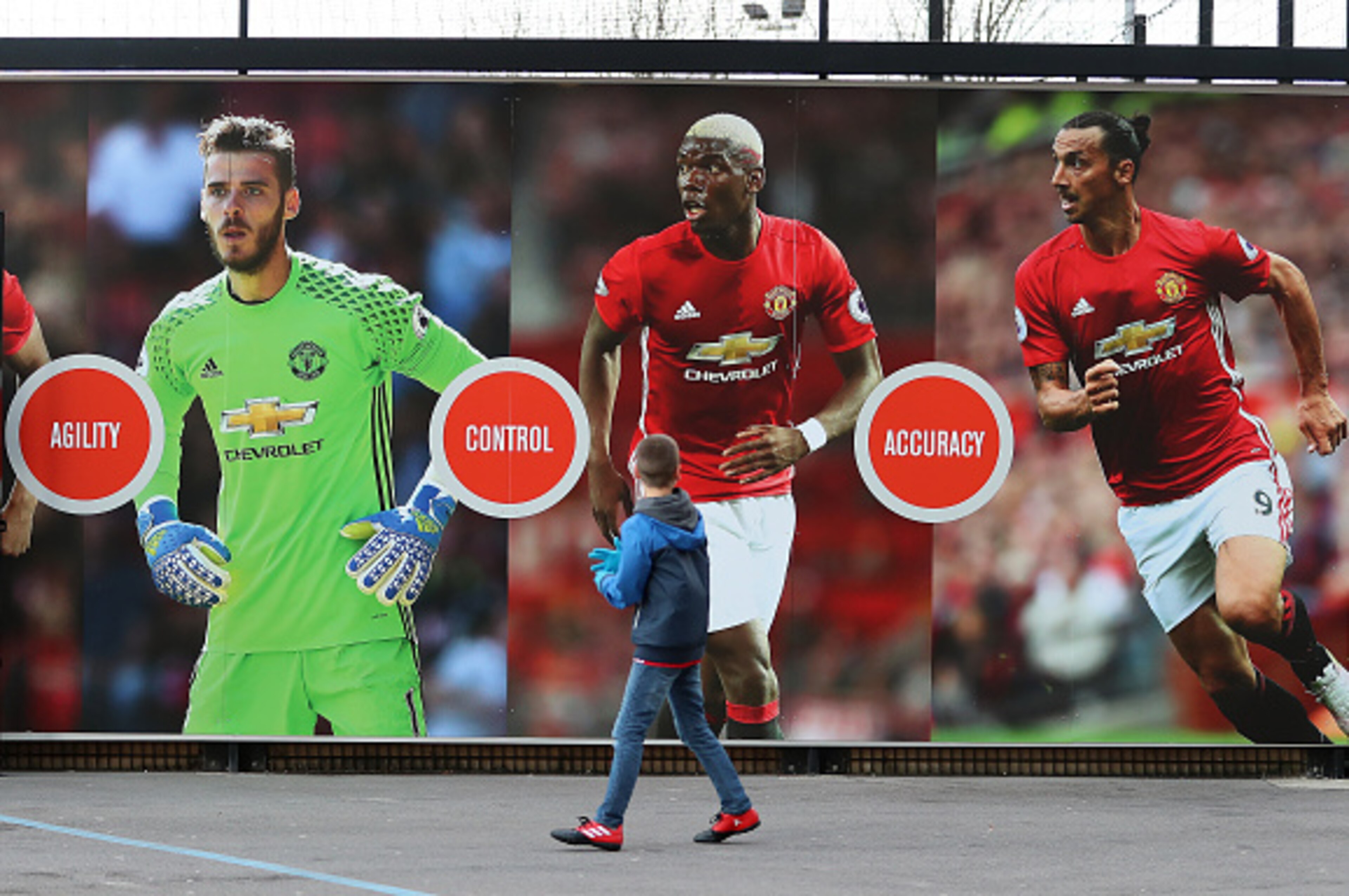 MANCHESTER, ENGLAND - DECEMBER 26: A young Manchester United supporter walks past a poster of Zlatan Ibrahimovic, Paul Pogba and David De Gea of Manchester United before the Premier League match between Manchester United and Sunderland at Old Trafford on 