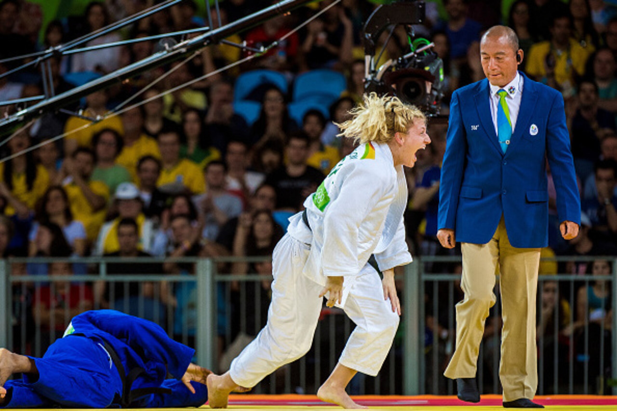 RIO DE JANEIRO, BRAZIL, AUGUST 11: Kayla Harrison of the United States (white) excitedly rises to her feet in front of referee Guoqiao Wang after arm-locking former world champion, Audrey Tcheumeo of France to win the u78kg gold medal during day 6 of the 