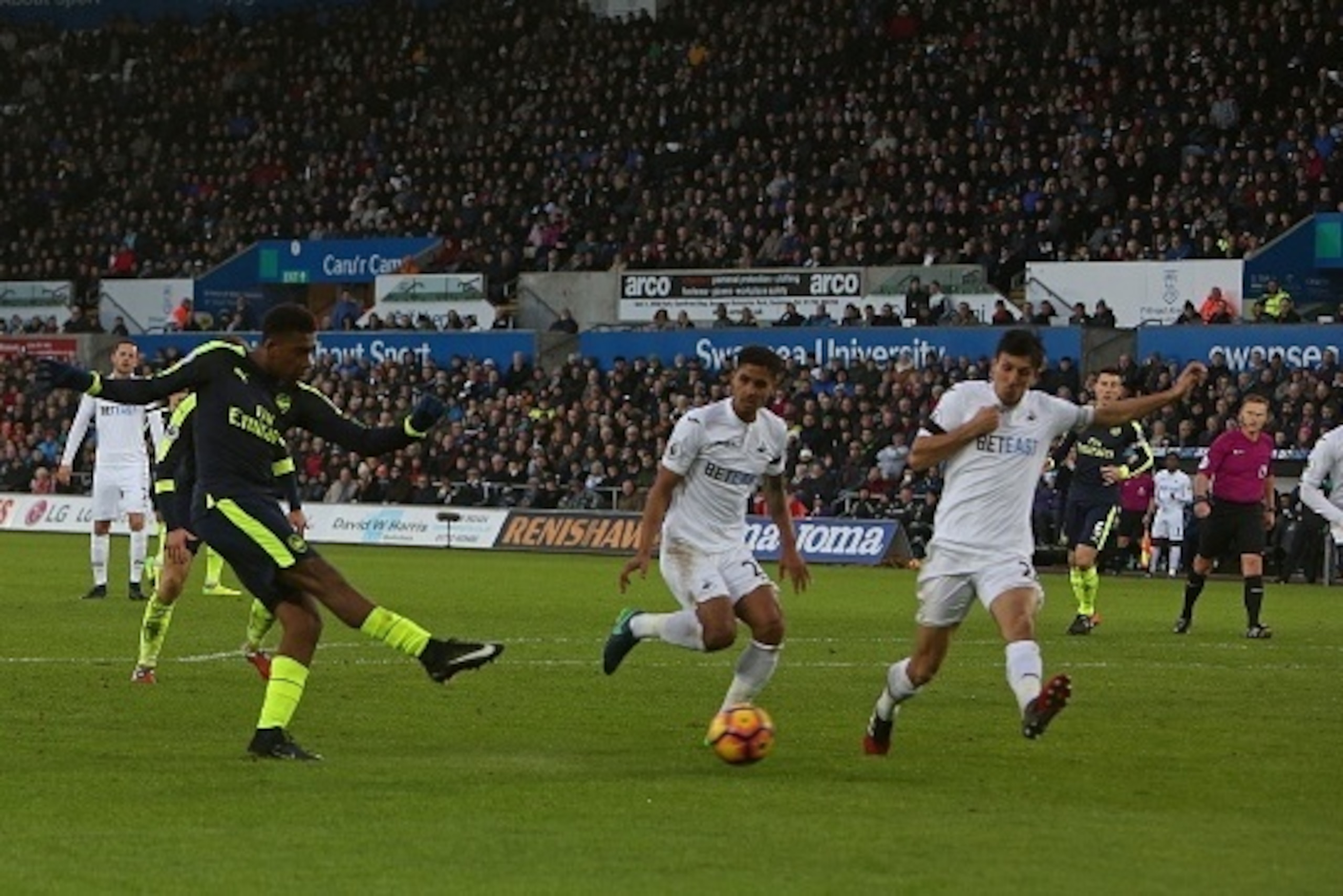 Arsenal's Nigerian striker Alex Iwobi (L) shoots, but has his shot deflected off of Swansea City's English midfielder Jack Cork, during the English Premier League football match between Swansea City and Arsenal at The Liberty Stadium in Swansea, south Wal Arsenal's Nigerian striker Alex Iwobi (L) shoots, but has his shot deflected off of Swansea City's English midfielder Jack Cork, during the English Premier League football match between Swansea City and Arsenal at The Liberty Stadium in Swansea, south Wal
