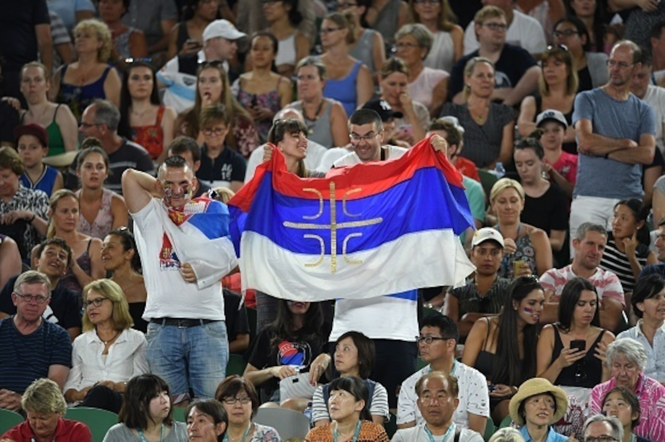 Fans of Serbia's Novak Djokovic hold the country's national flag during his men's singles match against Spain's Fernando Verdasco on day two of the Australian Open tennis tournament in Melbourne on January 17, 2017. / AFP / GREG WOOD / IMAGE RESTRICTED TO