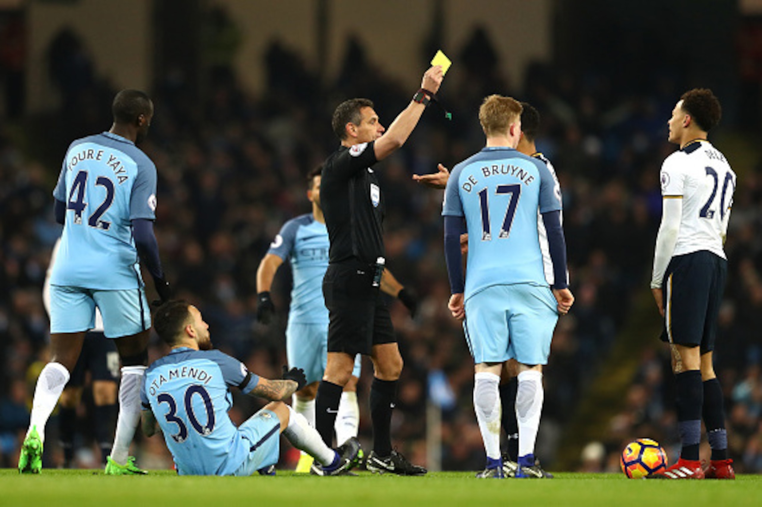 MANCHESTER, ENGLAND - JANUARY 21: Dele Alli of Tottenham Hotspur (R) is shown a yellow card by referee Andre Marriner (L) during the Premier League match between Manchester City and Tottenham Hotspur at the Etihad Stadium on January 21, 2017 in Manchester