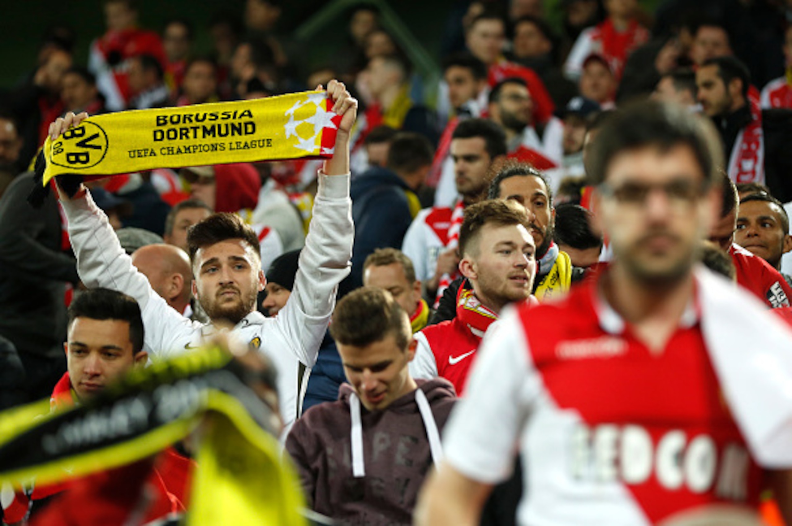 Monaco supporters with Borussia scarves react in the stadium after the match was postponed amid an explosion near the bus of Borussia Dortmund some 10km away from the stadium prior to the UEFA Champions League 1st leg quarter-final football match BVB Boru Monaco supporters with Borussia scarves react in the stadium after the match was postponed amid an explosion near the bus of Borussia Dortmund some 10km away from the stadium prior to the UEFA Champions League 1st leg quarter-final football match BVB Boru