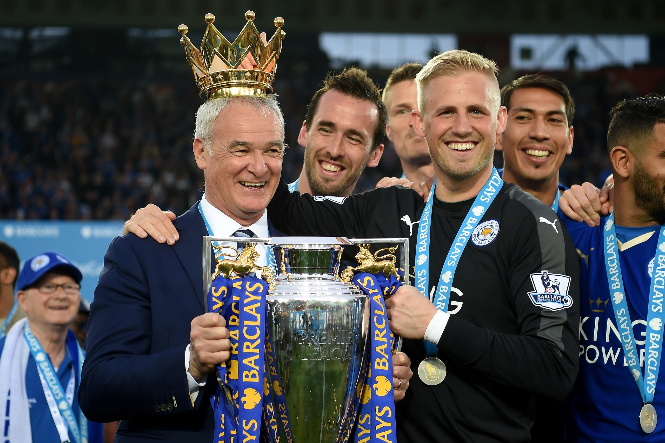 LEICESTER, ENGLAND - MAY 07:  Claudio Ranieri poses with the Premier League Trophy while Kasper Schmeichel puts the crown on the head of the manager as players and staffs celebrate the season champions after the Barclays Premier League match between Leice